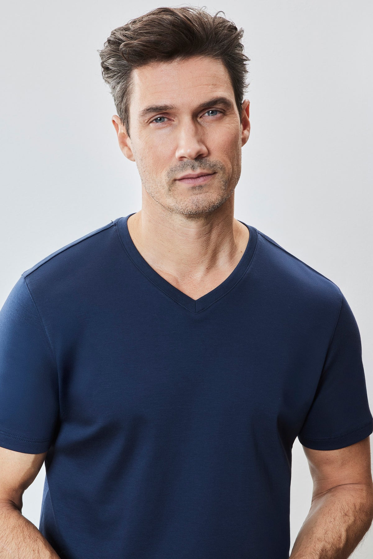 Man wearing navy blue V-neck t-shirt with short sleeves against a white background.