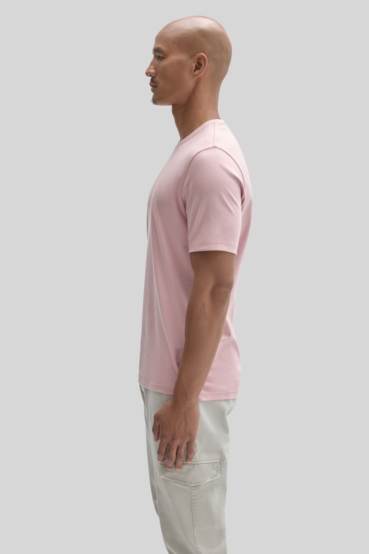 Man wearing a pink short-sleeve t-shirt and light-colored pants, shown in profile.