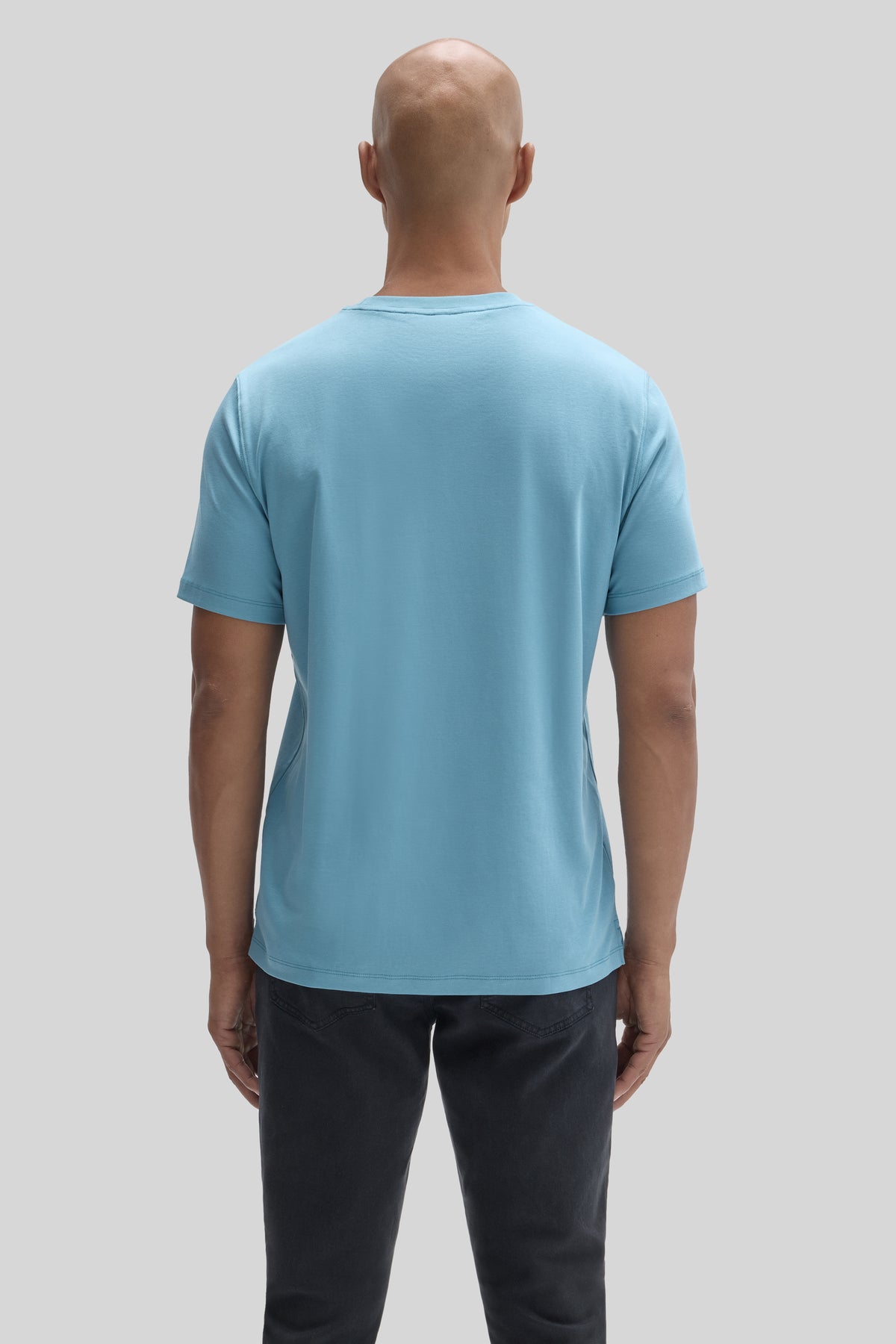 Man wearing light blue short-sleeve t-shirt, shown from back, paired with black pants.