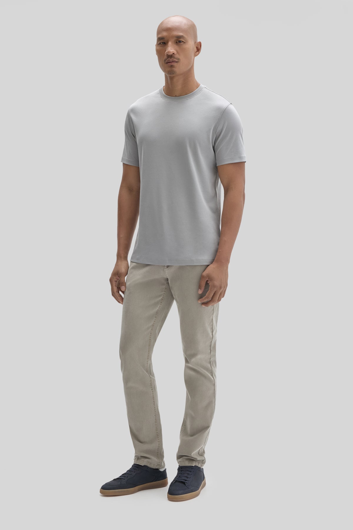 Man wearing light gray crew neck t-shirt with beige jeans and dark blue sneakers.