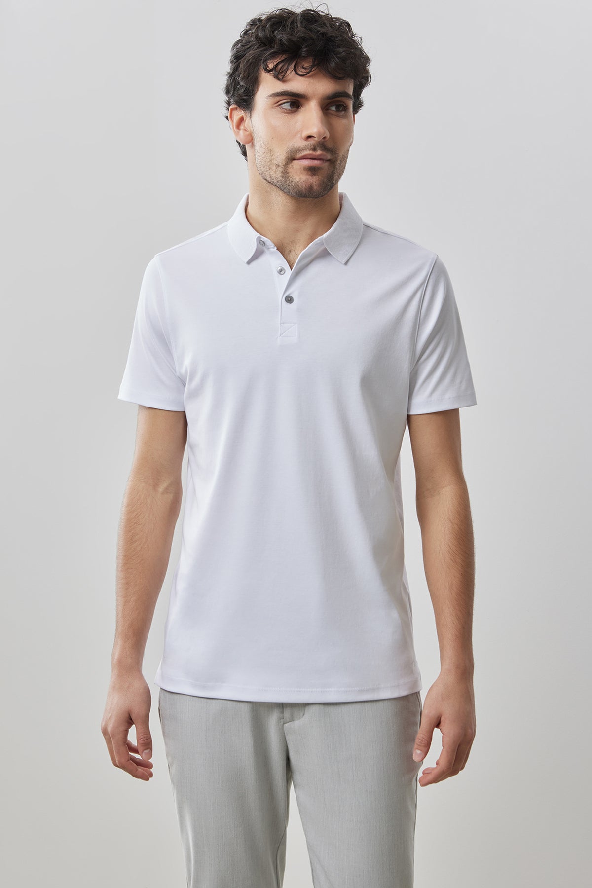Man wearing white short-sleeve polo shirt with collar and button placket, paired with light gray pants.