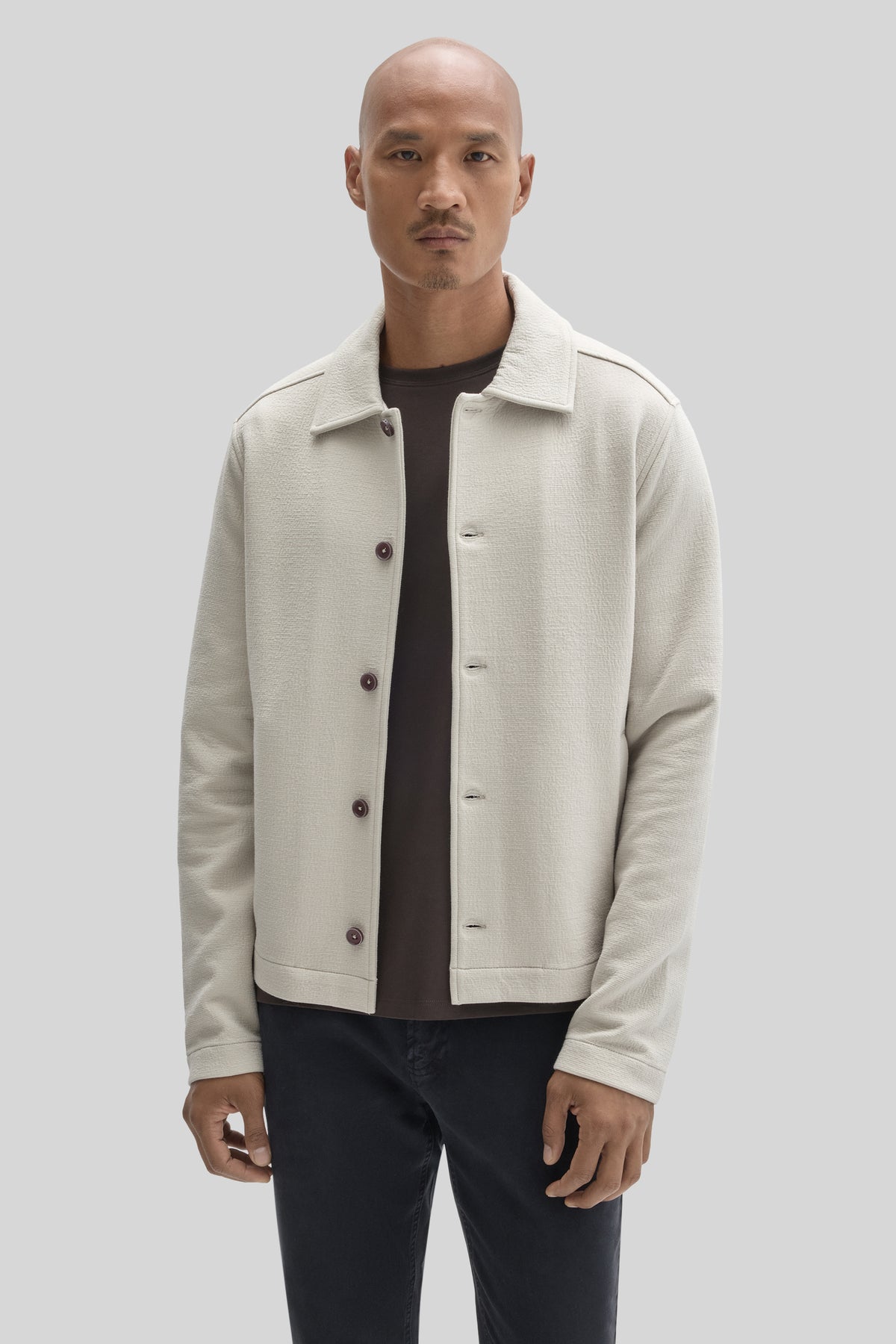 Cream buttoned jacket with collar worn over black shirt and dark trousers.