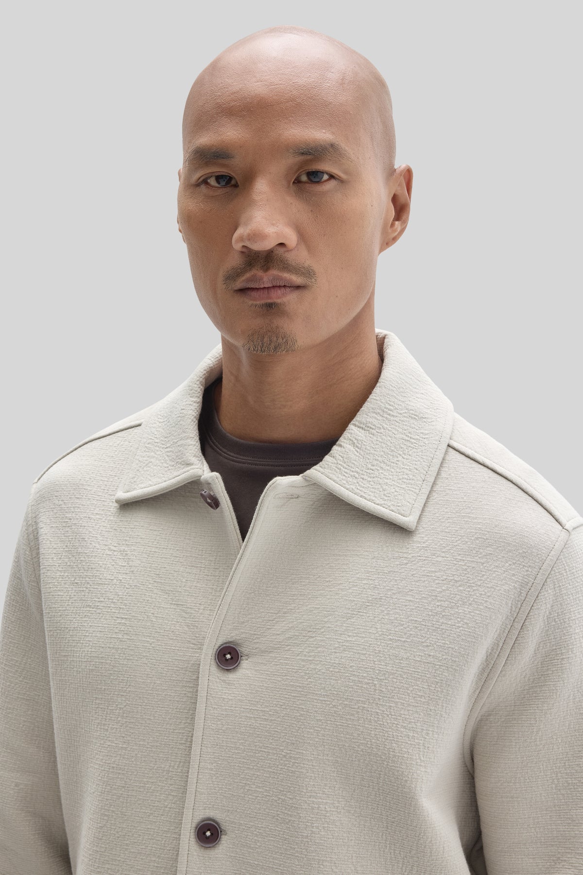 Man wearing cream-colored buttoned jacket with wide collar over dark shirt.