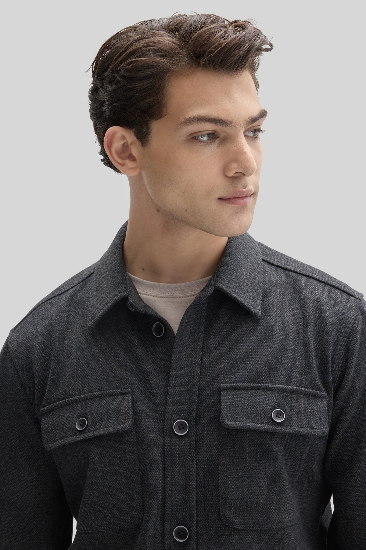 Man wearing charcoal gray buttoned jacket with chest pockets over tan undershirt, shown in profile view.