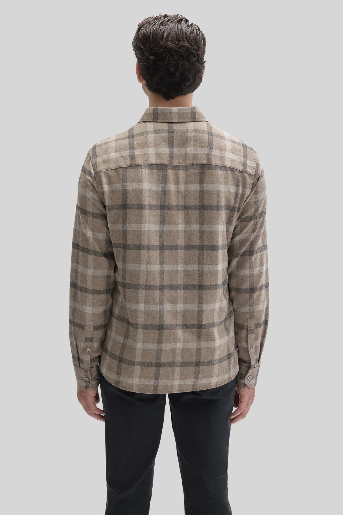 Man wearing tan and gray plaid flannel shirt with long sleeves and button cuffs, shown from back view.