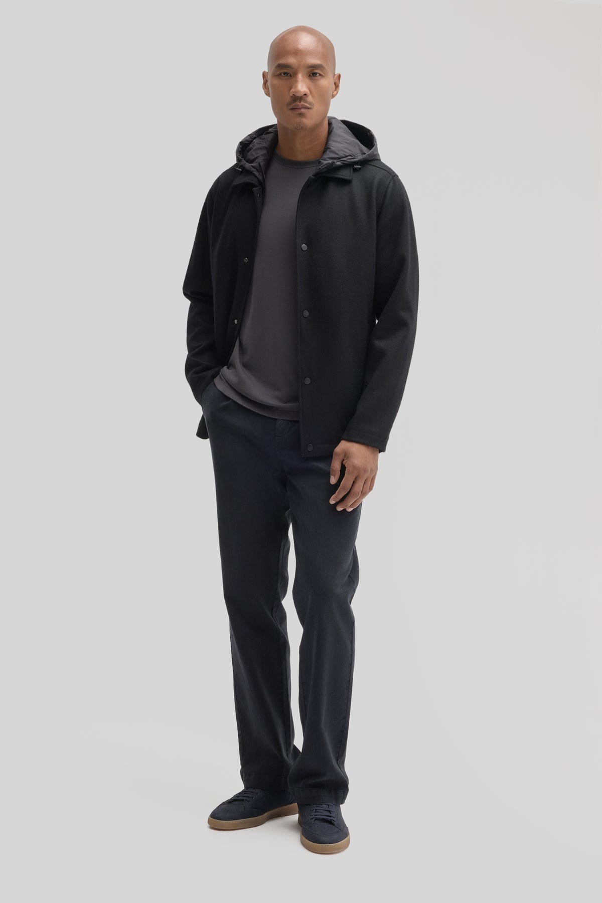 Man wearing black hooded car coat with button front over gray t-shirt and dark navy pants.