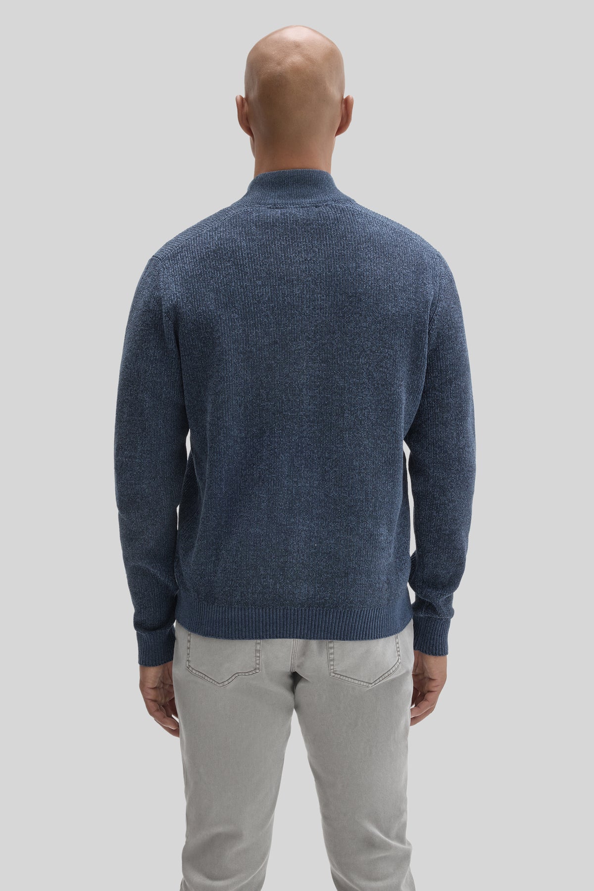Man wearing slate blue mock neck full zip sweater with ribbed cuffs and hem, paired with light gray jeans, shown from back.