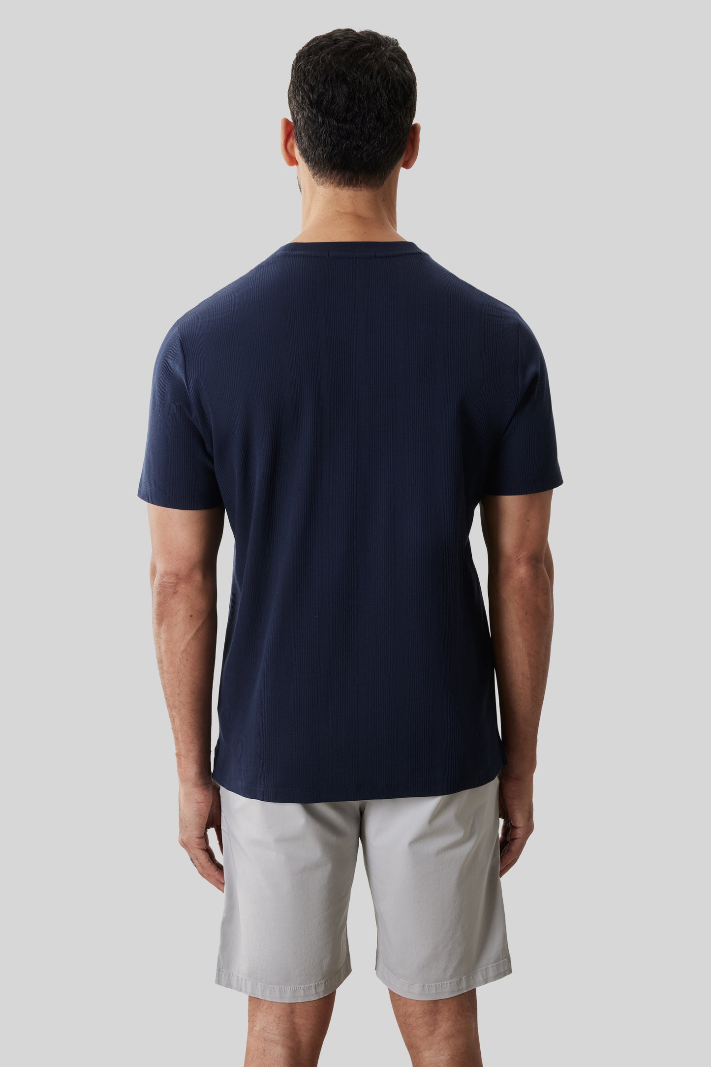 Man wearing navy ribbed short-sleeve t-shirt and light gray shorts, shown from behind.