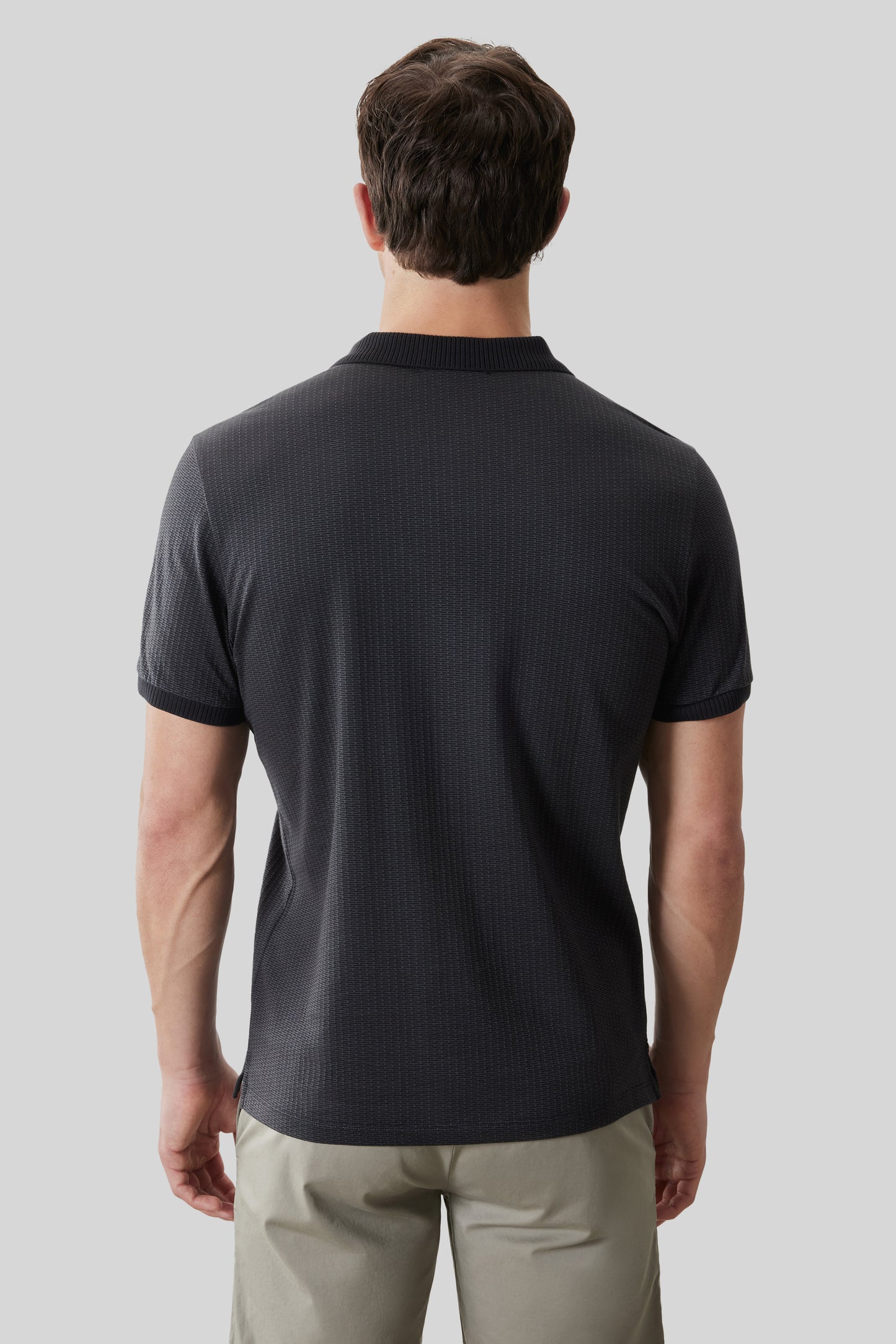 Man wearing dark gray short-sleeve polo shirt with ribbed texture and crew neckline, paired with tan pants.