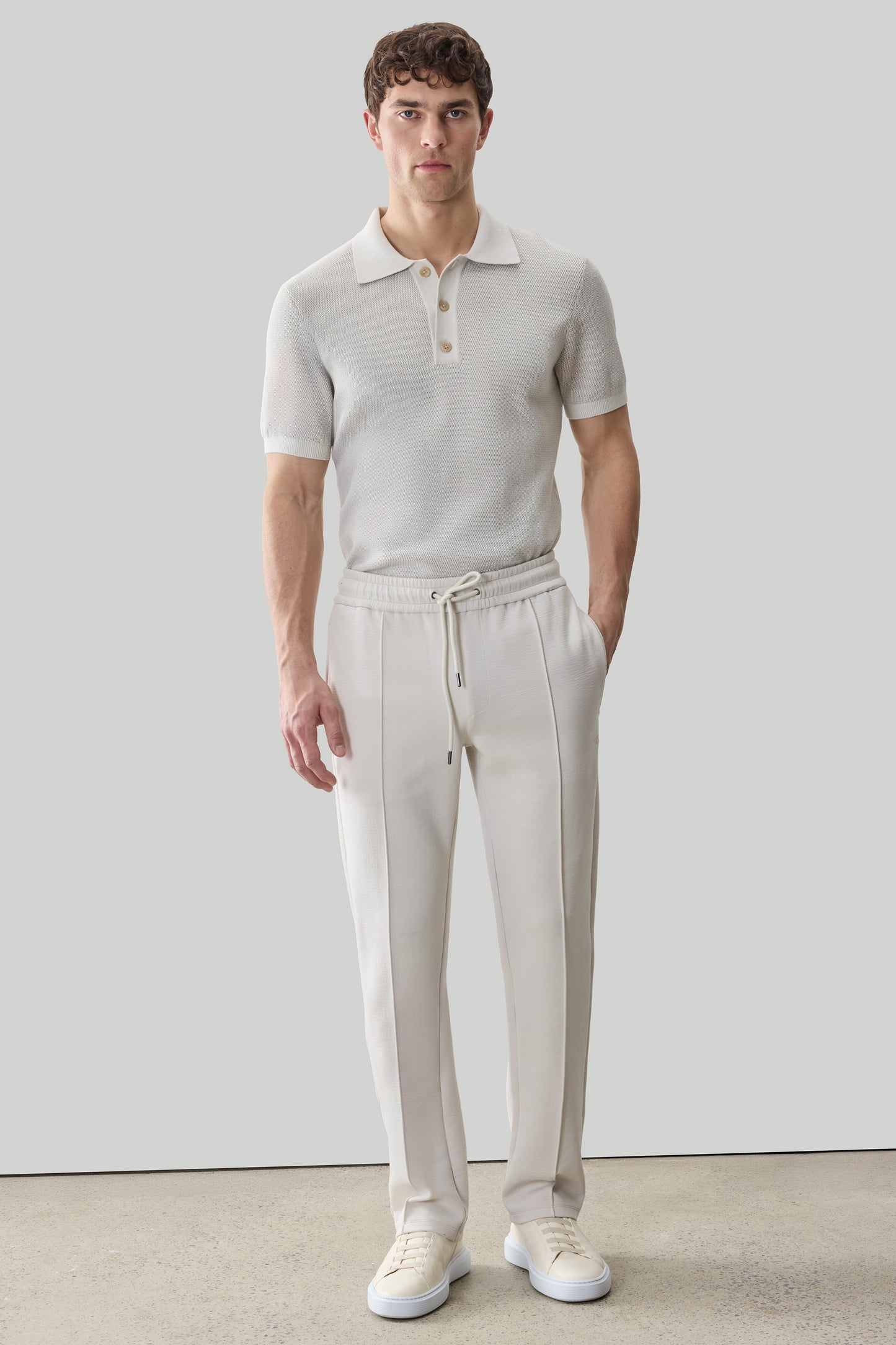 Man wearing beige Kenji jogger pants with drawstring waist and white polo shirt.