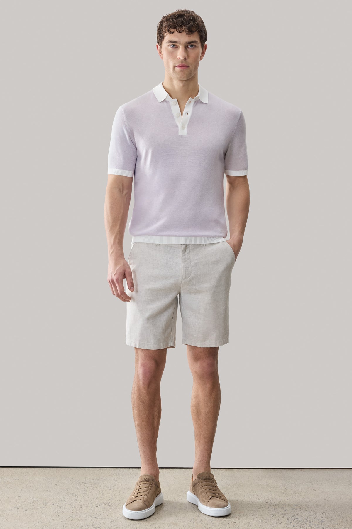 Man wearing lavender short-sleeve polo sweater with white collar and beige shorts.