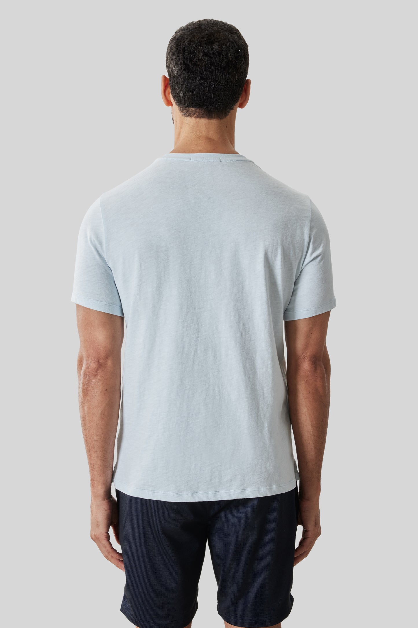 Man wearing light blue short-sleeve t-shirt and dark navy shorts, shown from behind.
