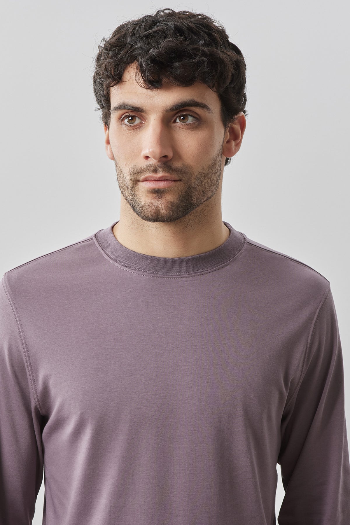 Man wearing mauve long-sleeve crew neck sweatshirt against neutral background.