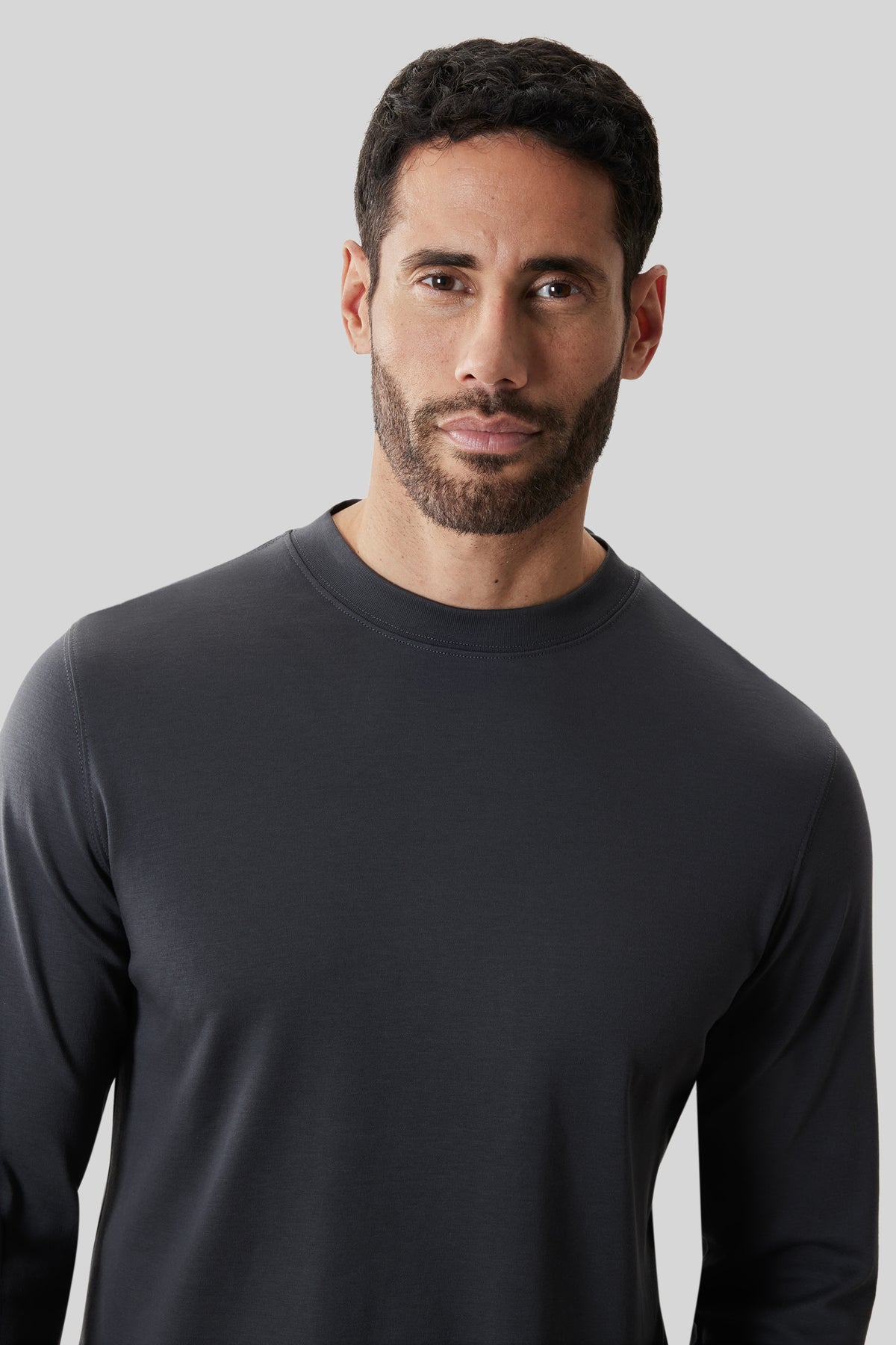 Man wearing a dark gray long-sleeve crew neck sweater against a light gray background.