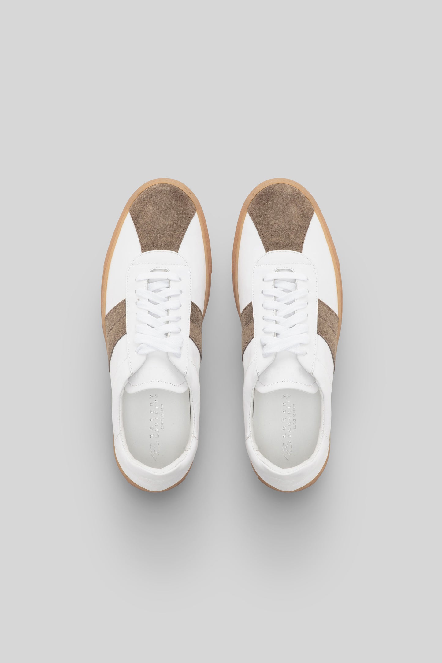 White sneakers with tan and olive suede stripe panels, white laces, and gum sole, shown from above.