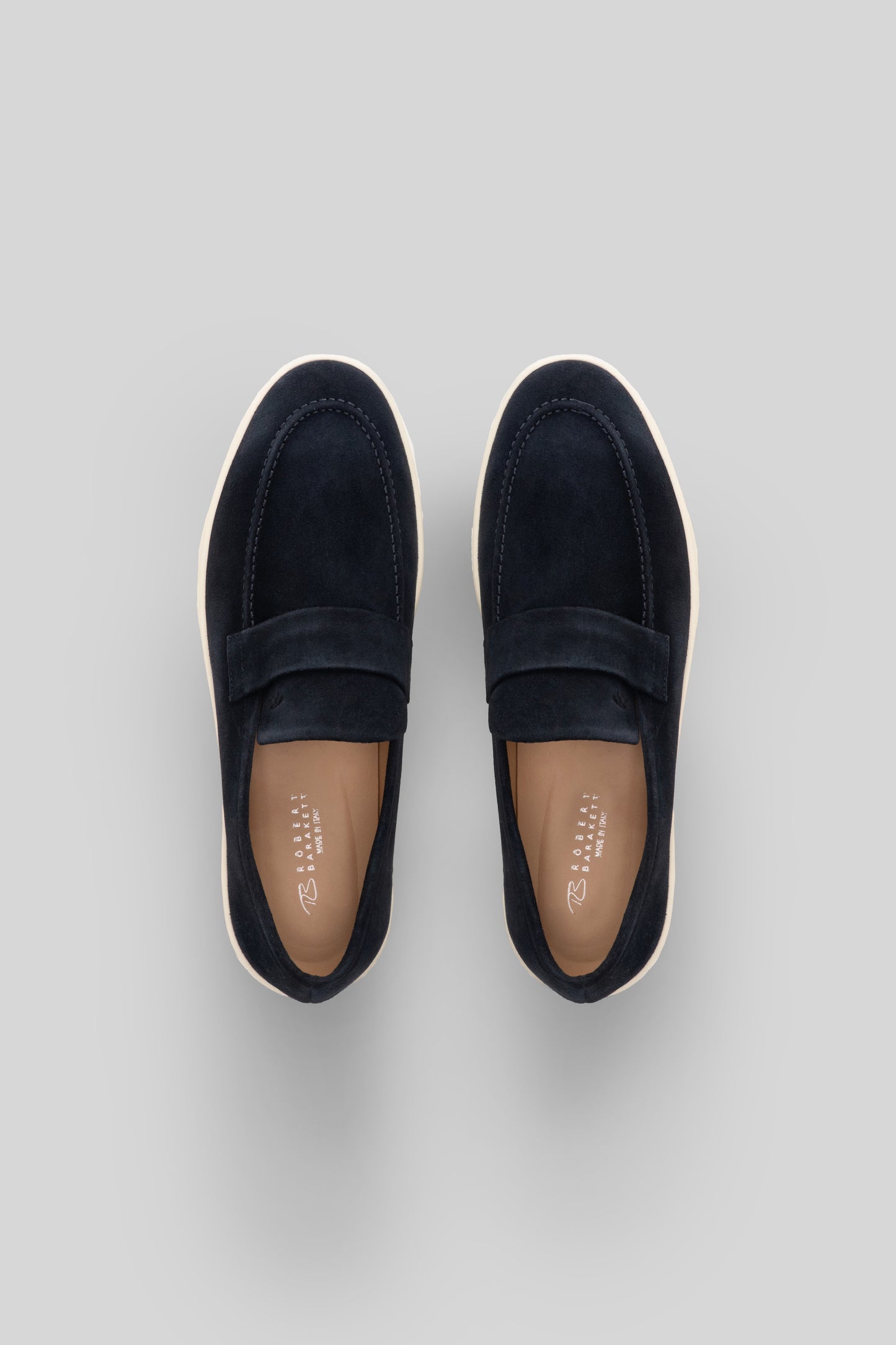 Navy suede loafer-style sneaker with cream rubber sole, shown from above.