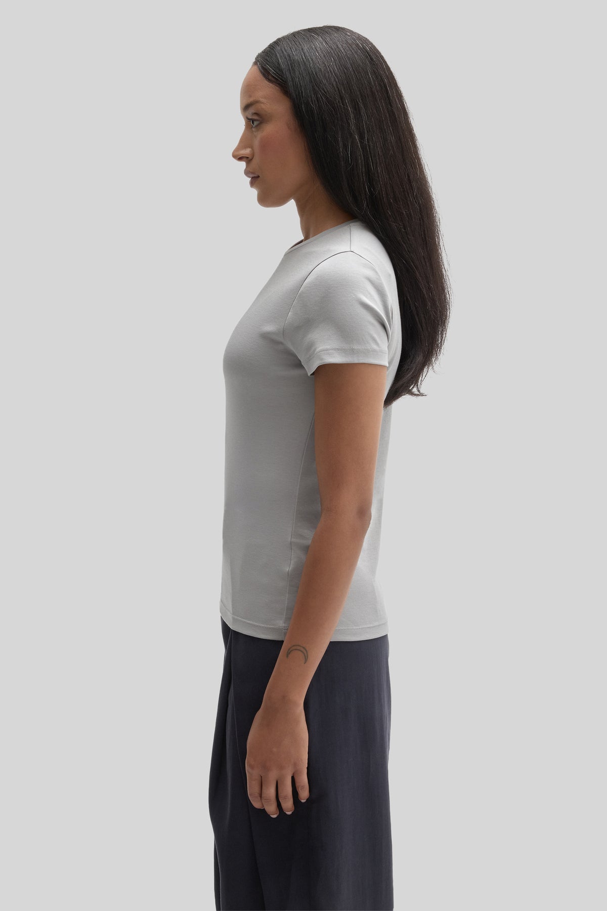 Woman wearing white short-sleeve t-shirt with dark trousers, shown in side profile view.