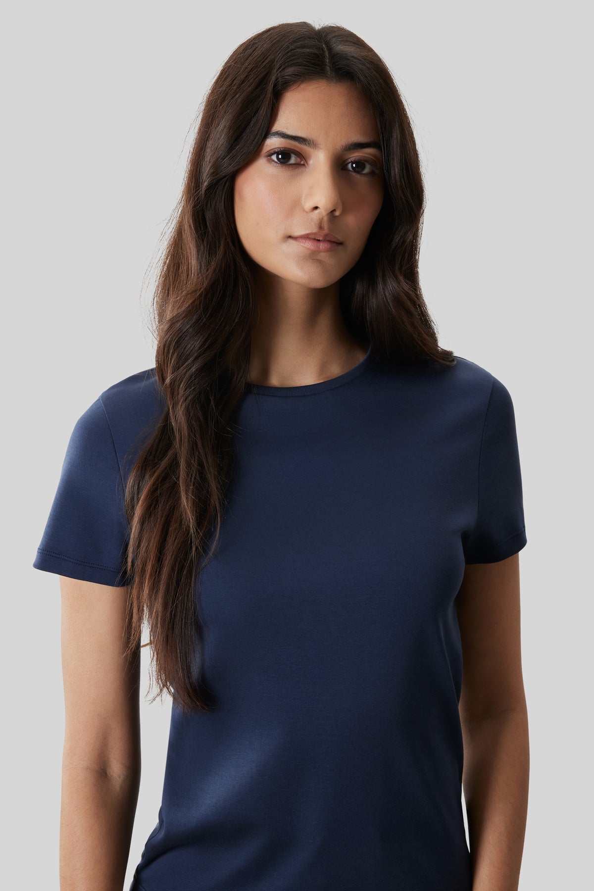 Woman wearing a dark navy short-sleeved crew neck t-shirt against a light gray background.