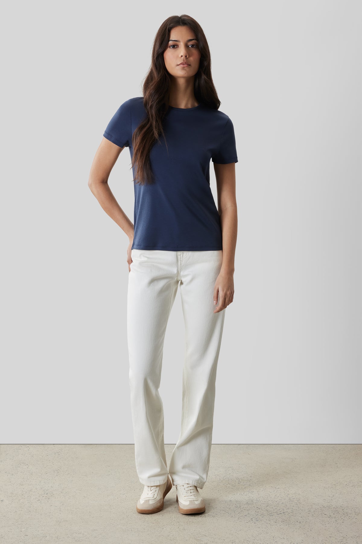 Woman wearing a navy blue short-sleeve crew neck t-shirt with white straight-leg pants and white sneakers.