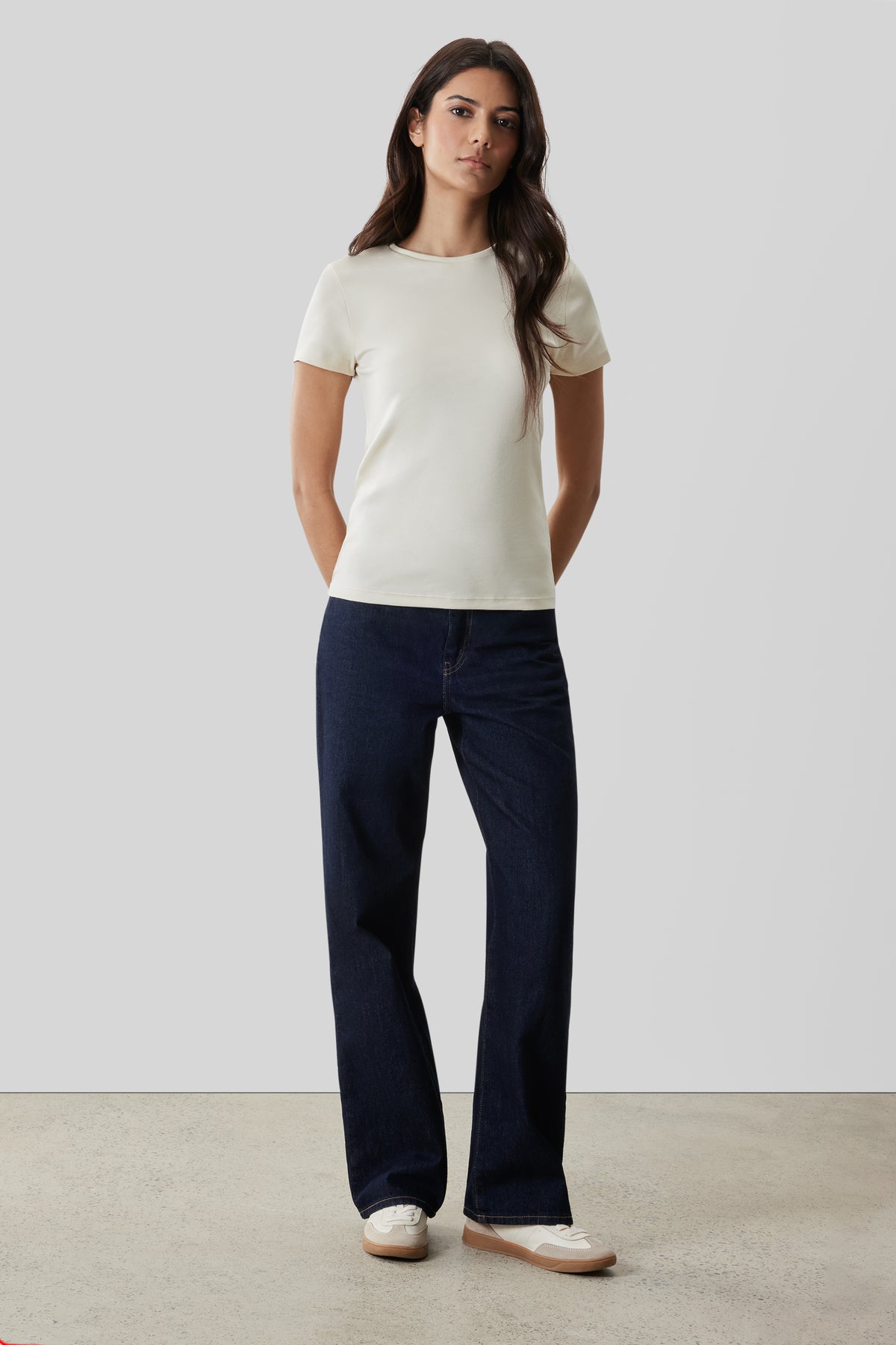 Woman wearing cream short-sleeve crew neck tee with dark navy denim jeans and white sneakers.