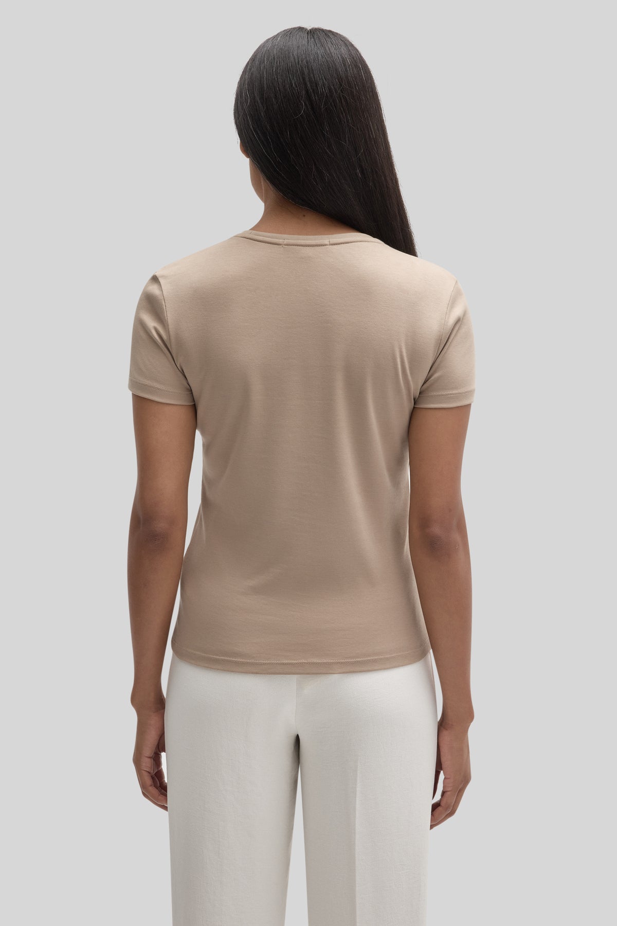 Woman wearing a beige short-sleeve crew neck tee with white pants, shown from behind.