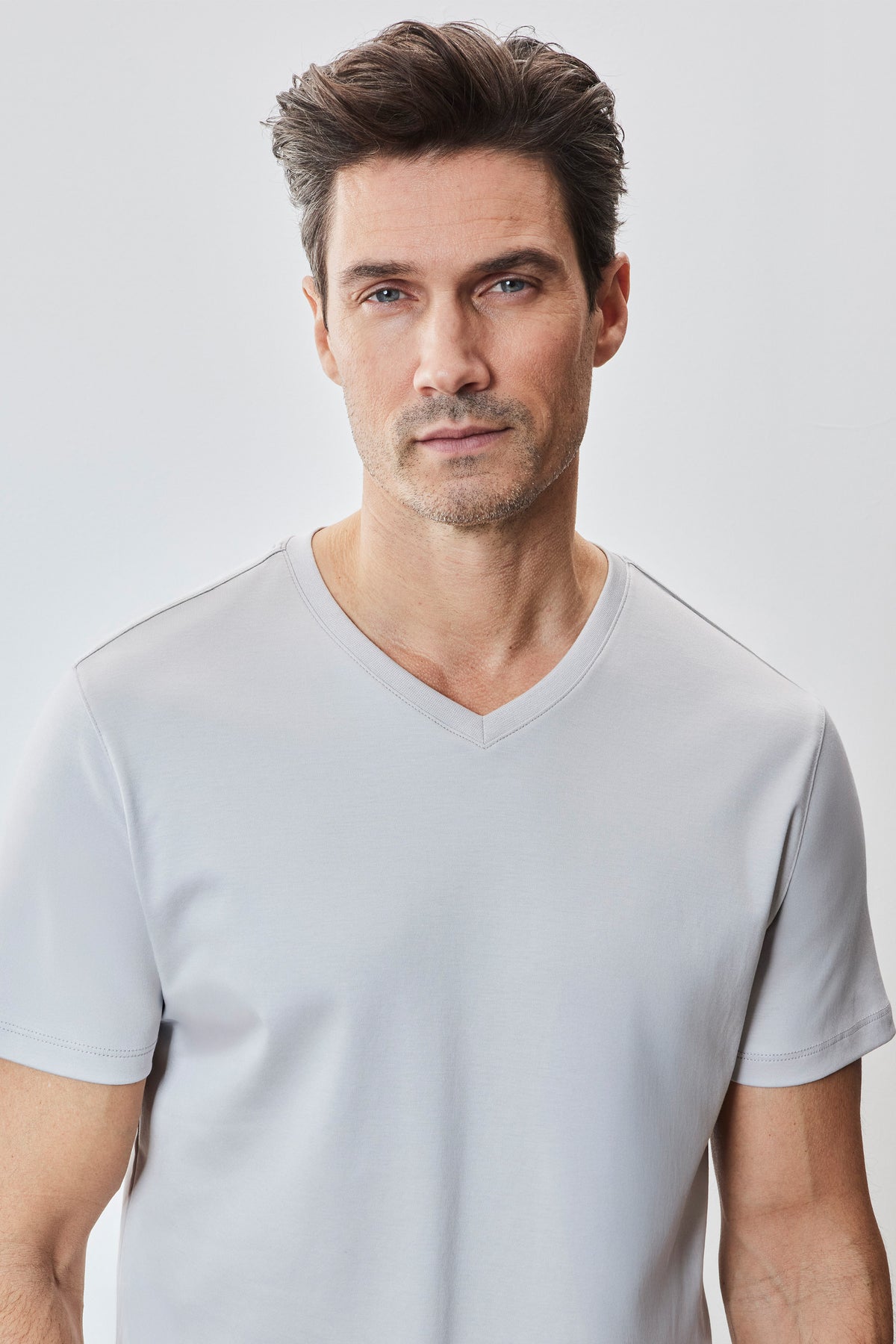 Man wearing light gray V-neck short-sleeve t-shirt against white background.