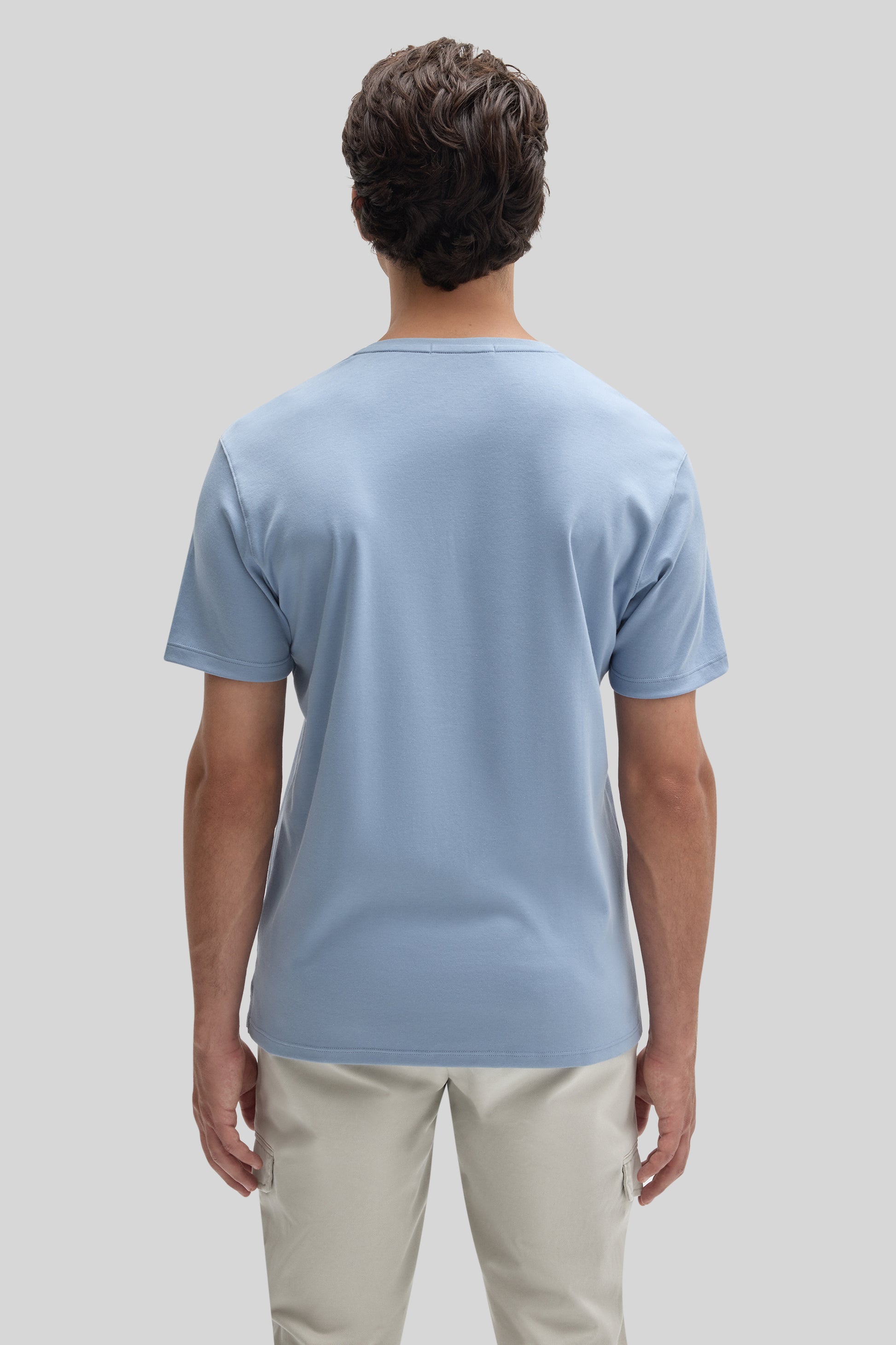 Man wearing light blue V-neck t-shirt with short sleeves and beige cargo pants, shown from behind.