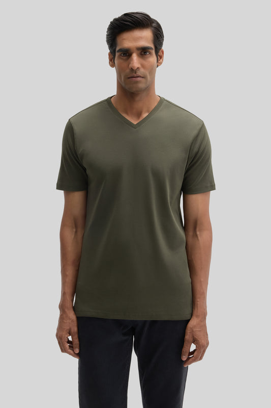 Man wearing olive green V-neck short-sleeve t-shirt with dark pants against neutral background.
