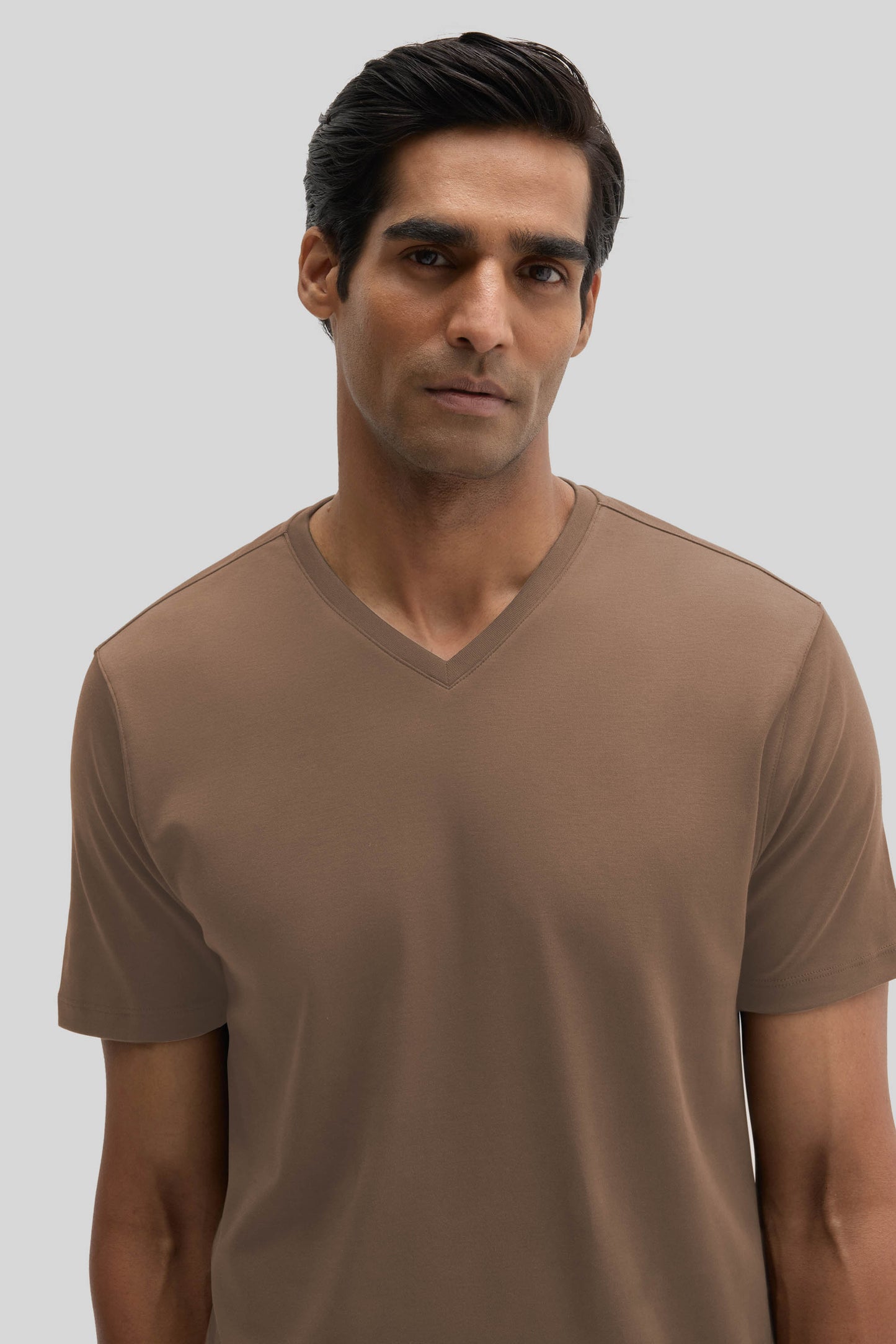 Man wearing taupe V-neck short-sleeve t-shirt against neutral background.
