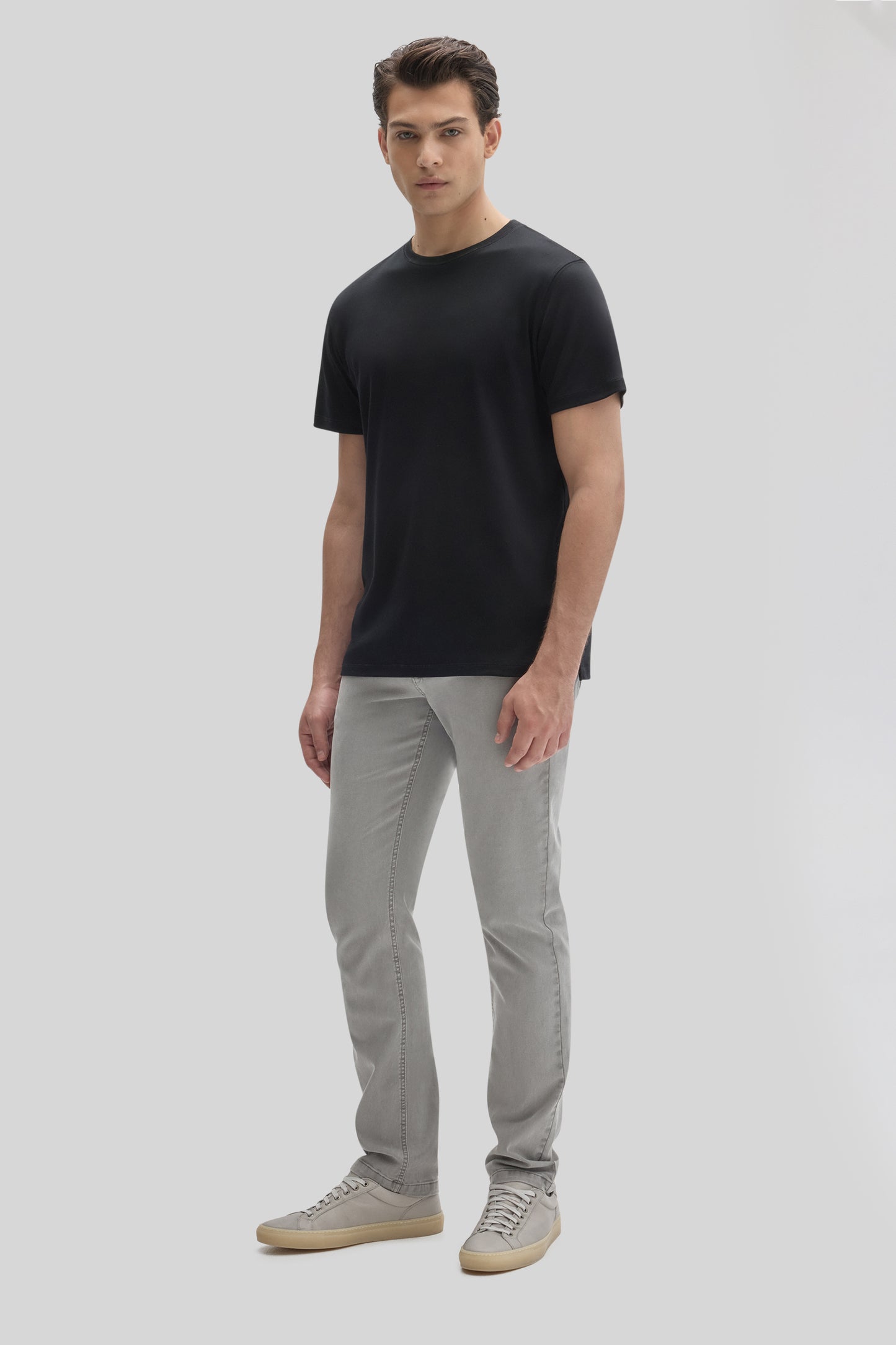 Man wearing black short-sleeve crew neck t-shirt with gray jeans and gray sneakers.