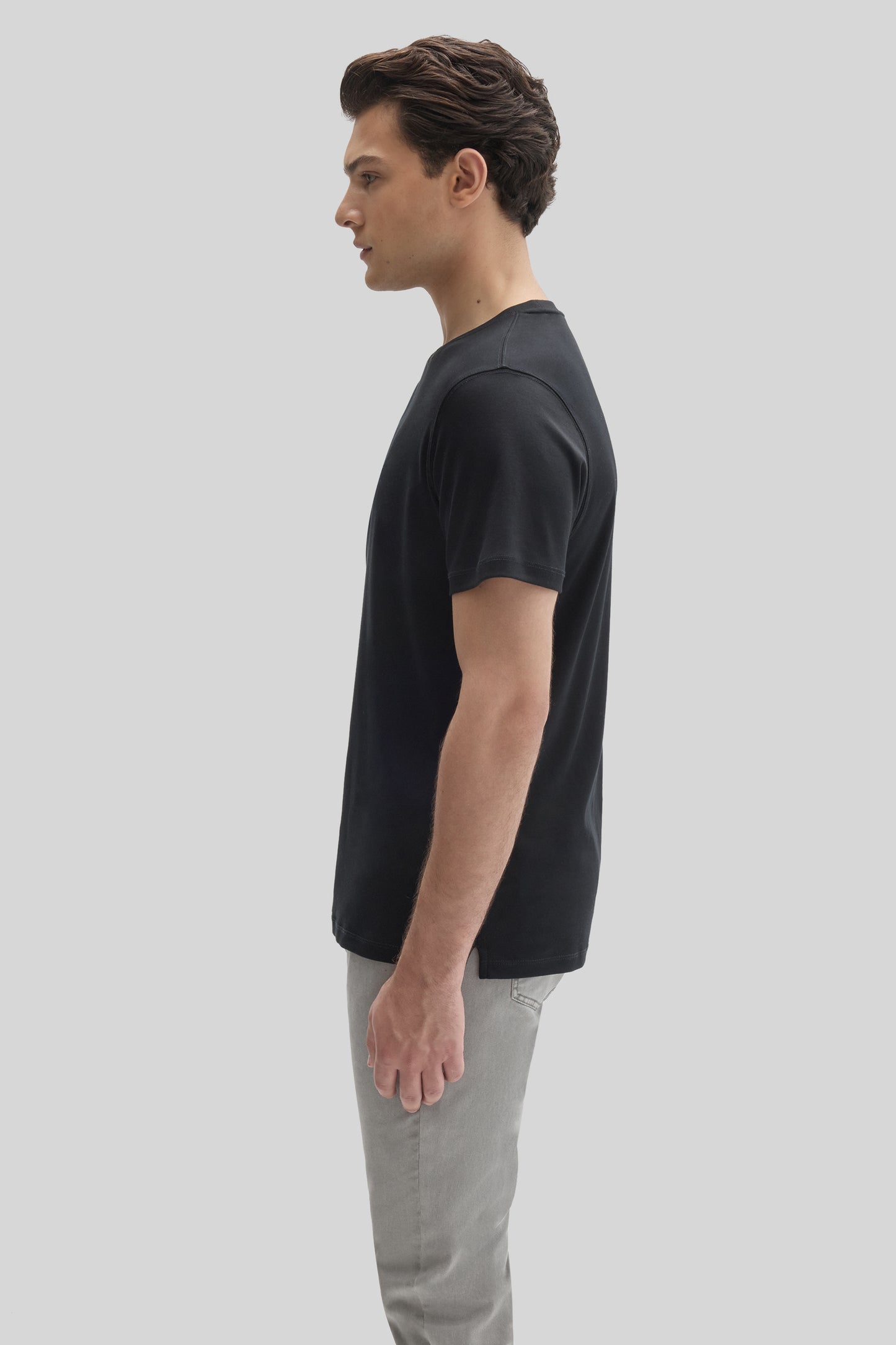 Man wearing black short-sleeve t-shirt with gray pants, shown in side profile.
