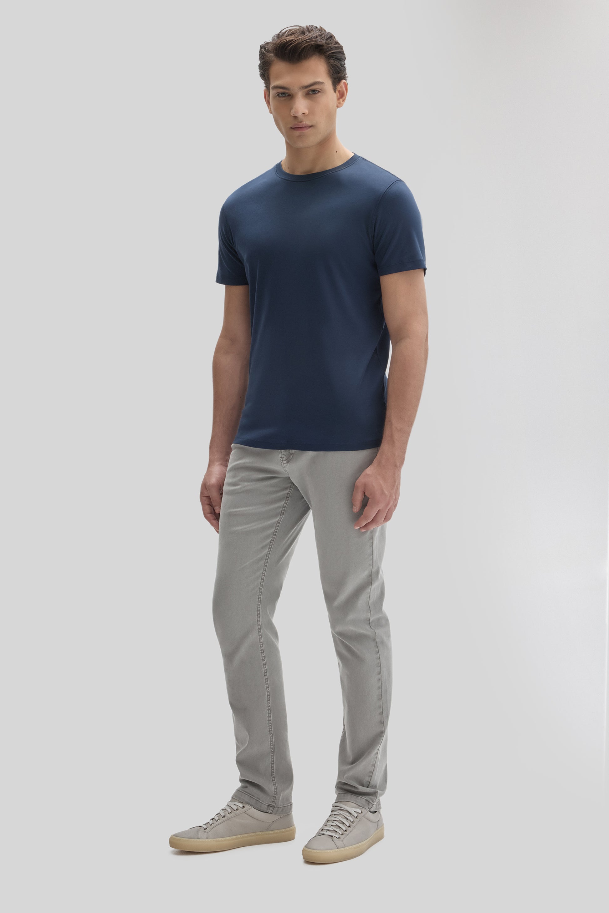 Man wearing a navy blue short-sleeve crew neck tee with gray jeans and light gray sneakers.