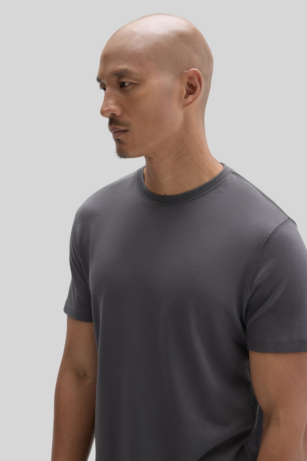 Man wearing a charcoal gray crew neck t-shirt, shown in profile view against a white background.