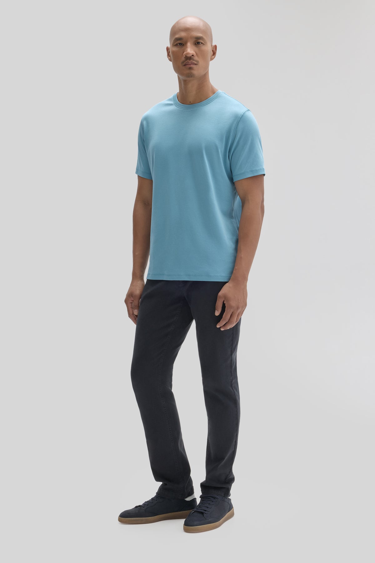 Man wearing light blue short-sleeve crewneck tee with black jeans and dark sneakers.