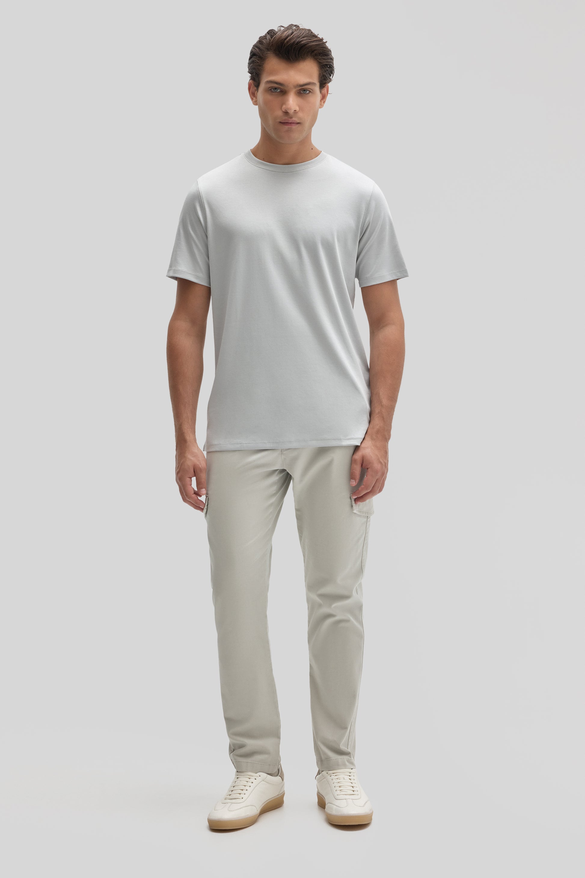 Man wearing light gray crew neck t-shirt with beige cargo pants and cream sneakers.