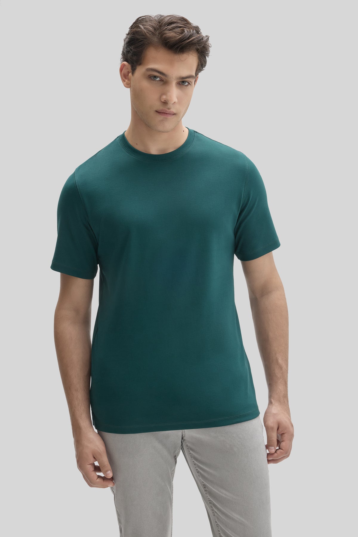 Man wearing a teal crew neck short-sleeve t-shirt with light gray pants against a neutral background.