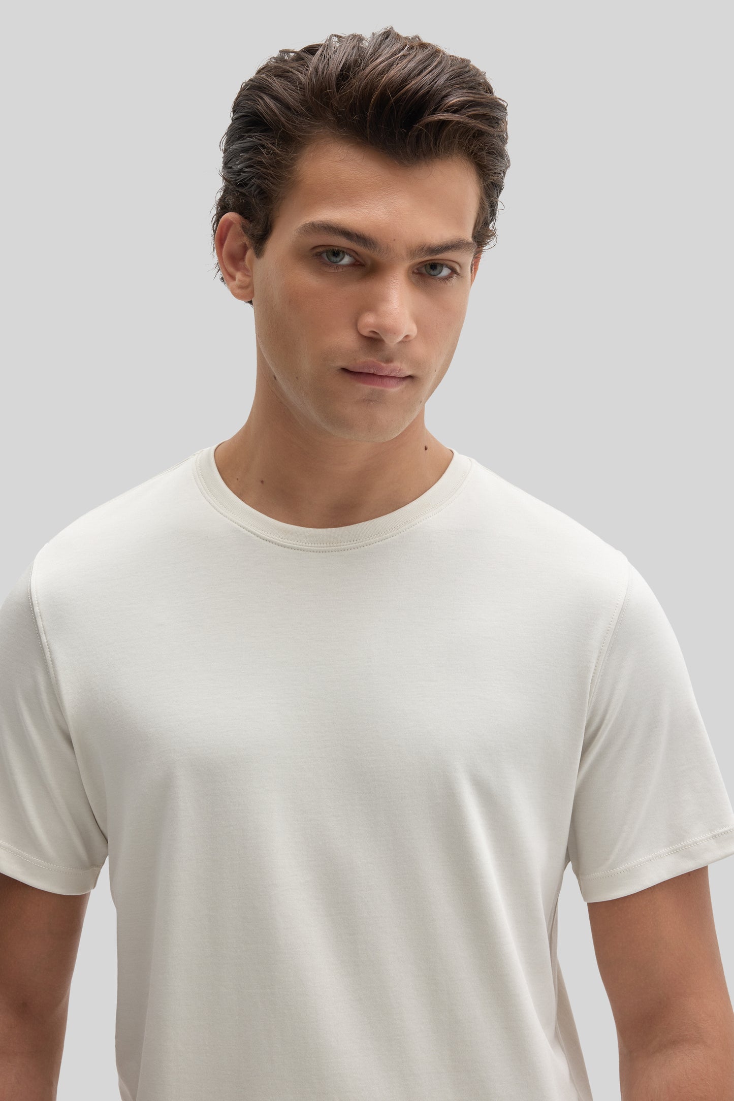 Man wearing a cream-colored crew neck t-shirt with short sleeves against a neutral background.
