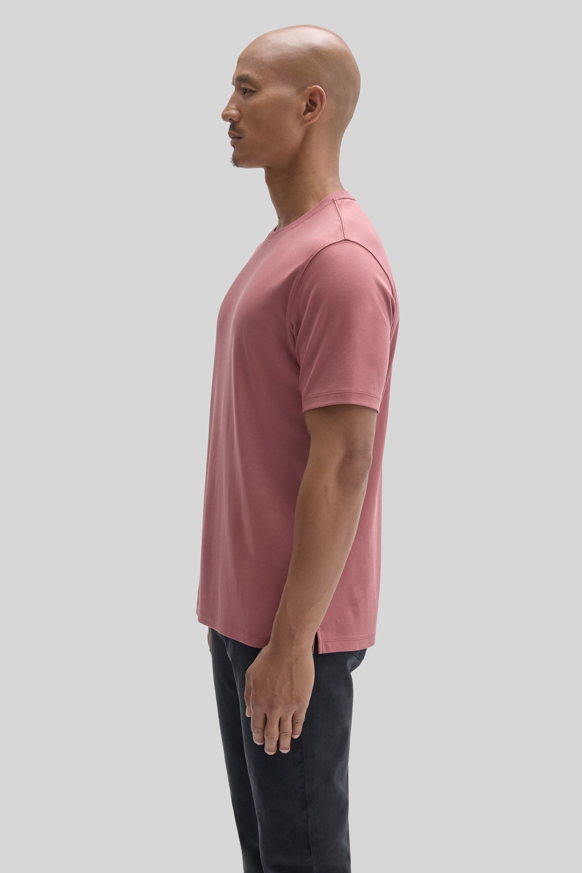 Man wearing a mauve pink short-sleeve t-shirt with black pants, shown in profile view.