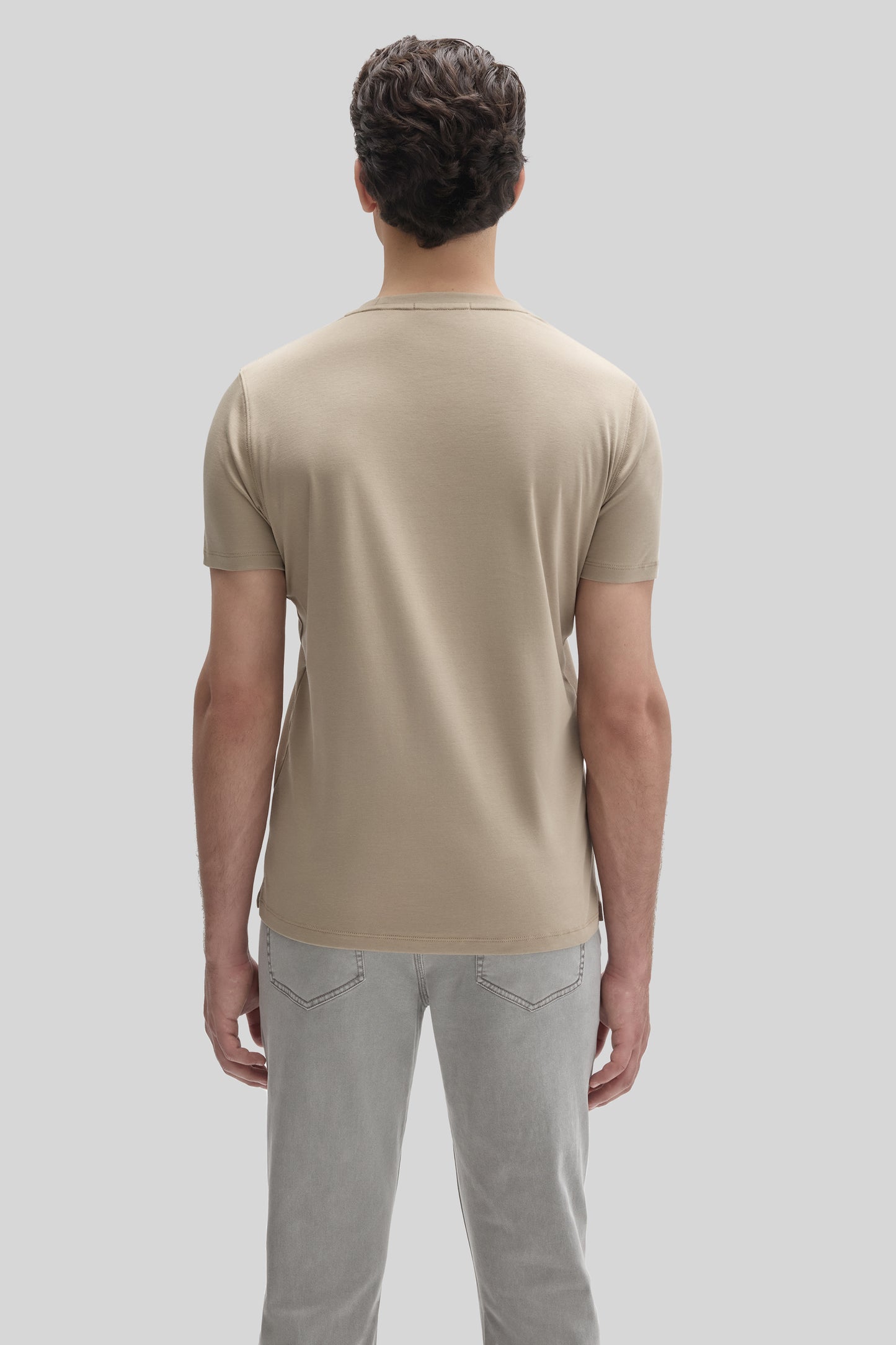 Man wearing a beige short-sleeve t-shirt and light gray jeans, shown from the back.