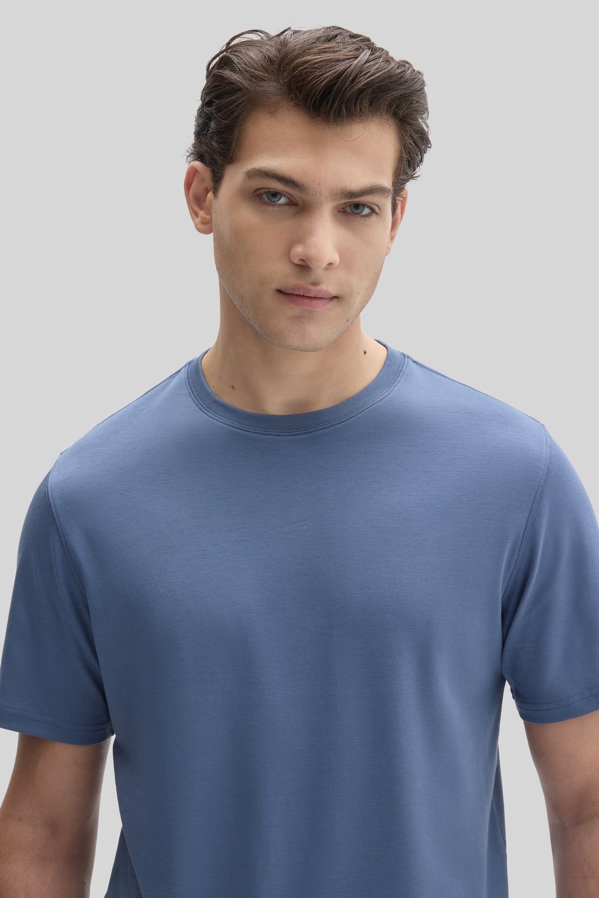 Man wearing a blue crew neck t-shirt with short sleeves against a light gray background.