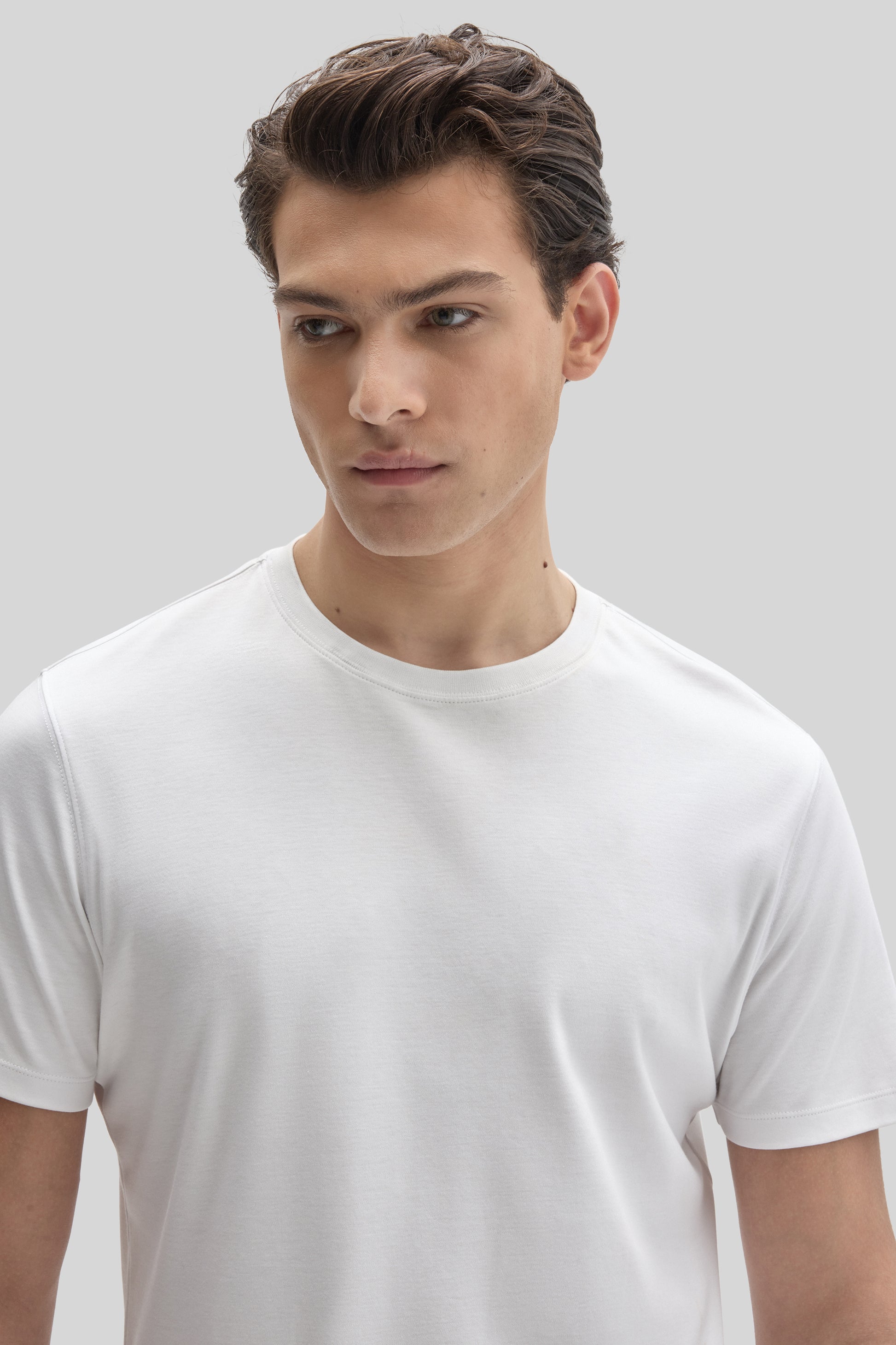 Man wearing a white crew neck short-sleeve t-shirt against a neutral background.