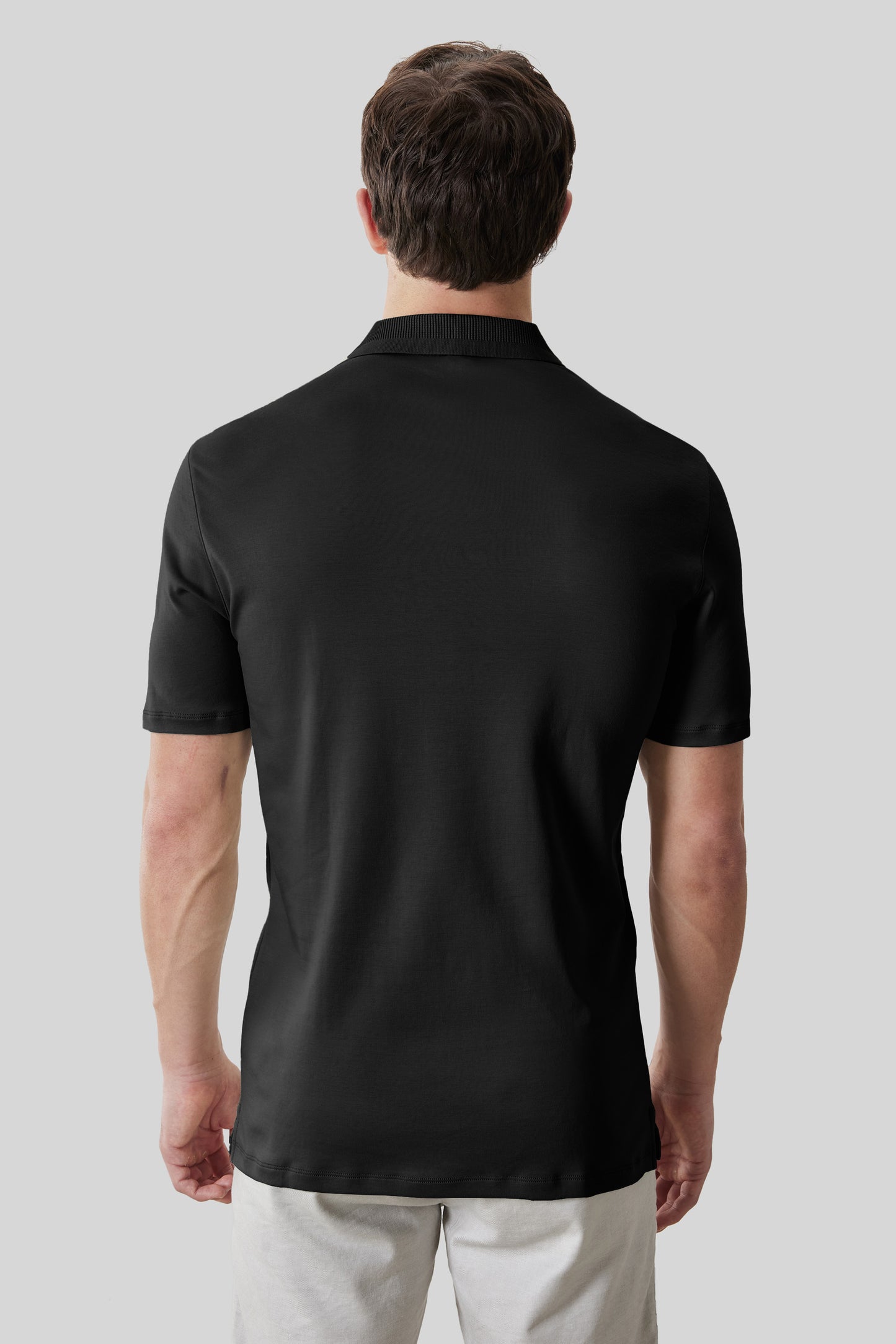 Black textured collar polo shirt with short sleeves, shown from back on male model wearing white pants.