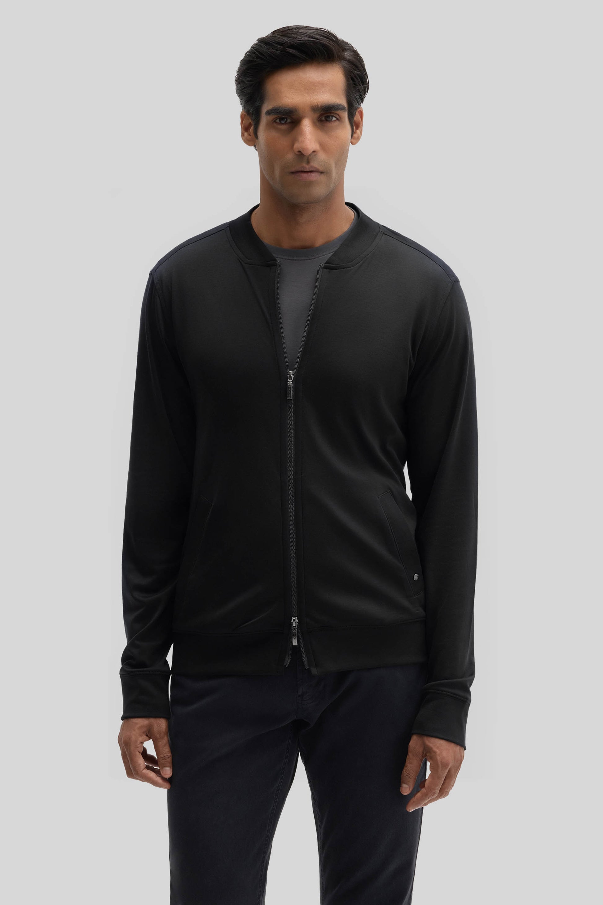 Man wearing black baseball jacket with full-length zip and ribbed cuffs over dark pants.