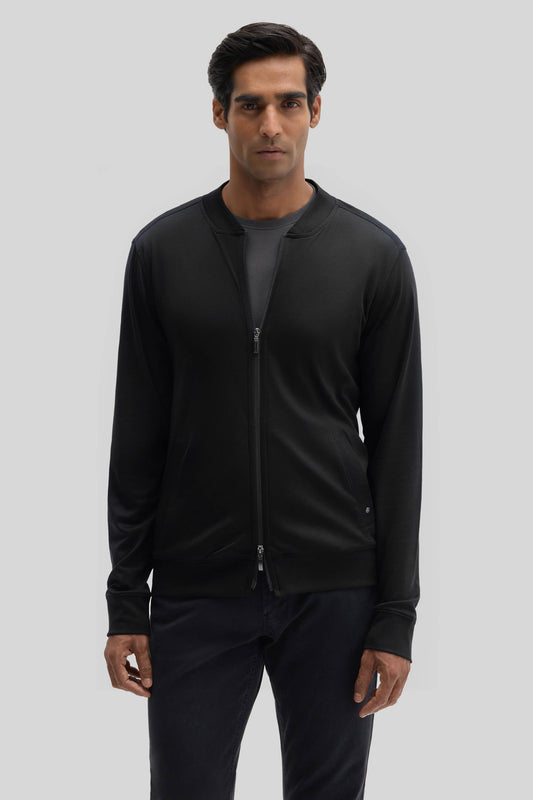 Man wearing black baseball jacket with full-length zip and ribbed cuffs over dark pants.