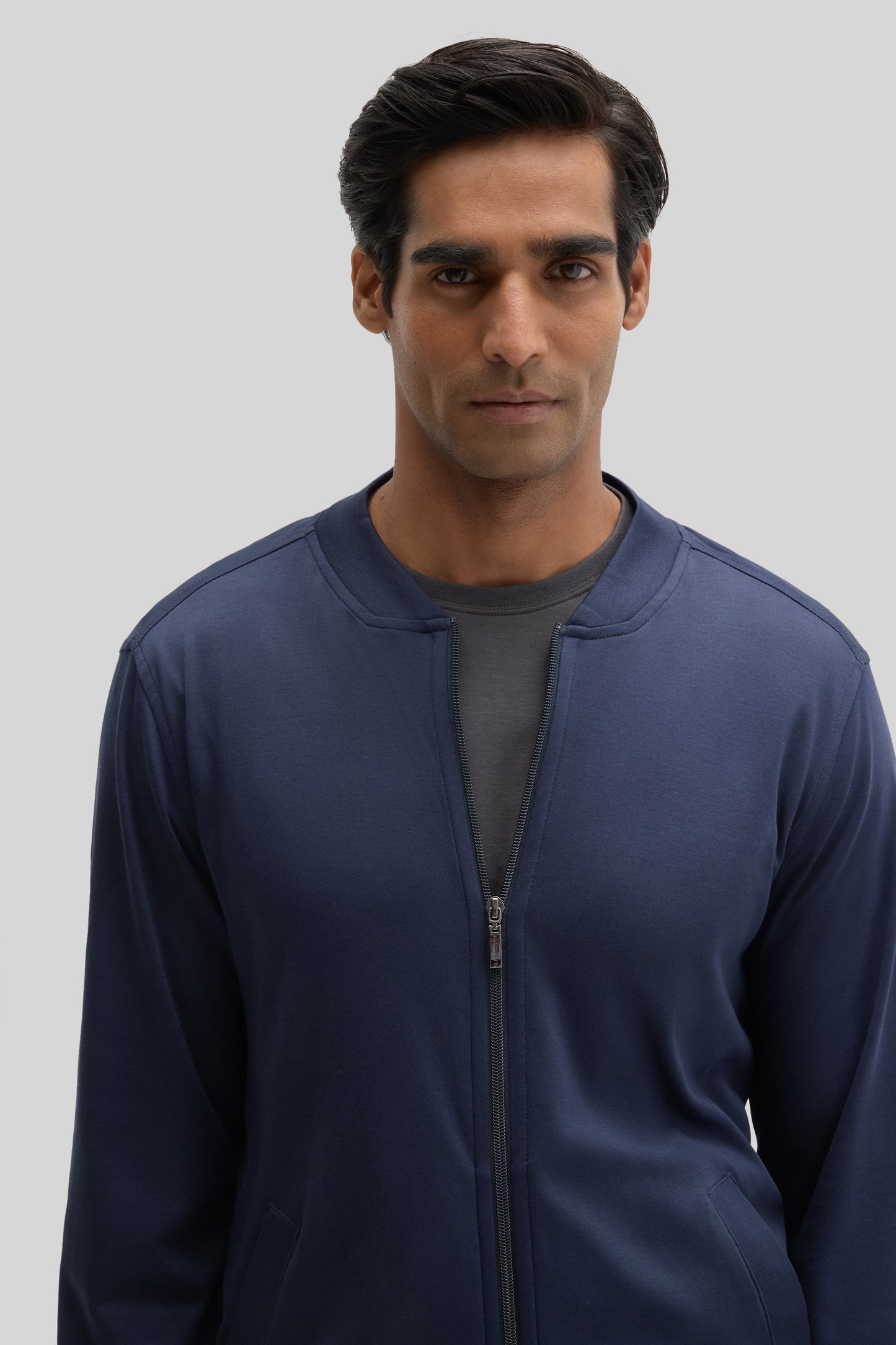 Navy blue baseball jacket with front zip closure and patch pockets worn by a man.