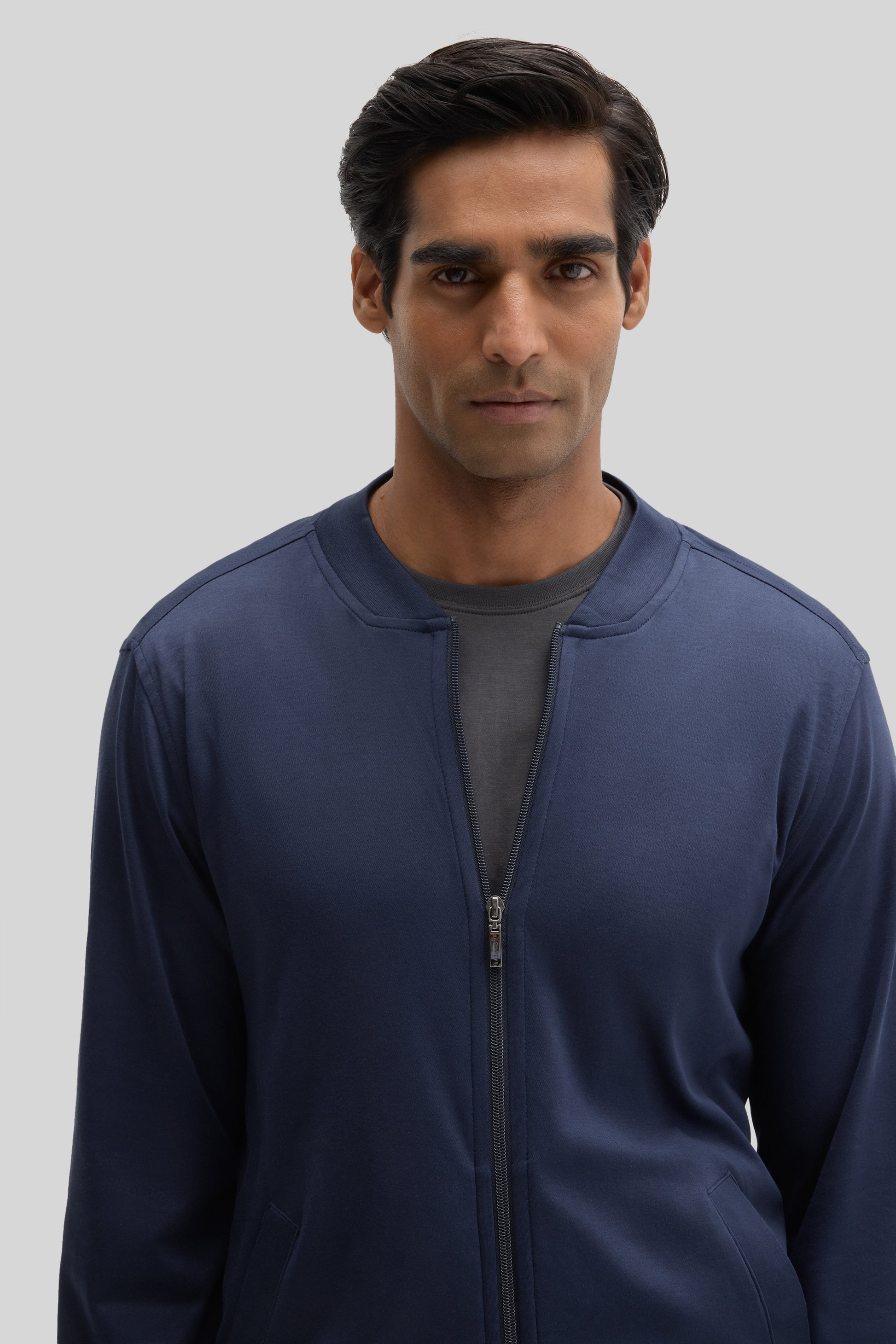Navy blue baseball jacket with front zip closure and patch pockets worn by a man.