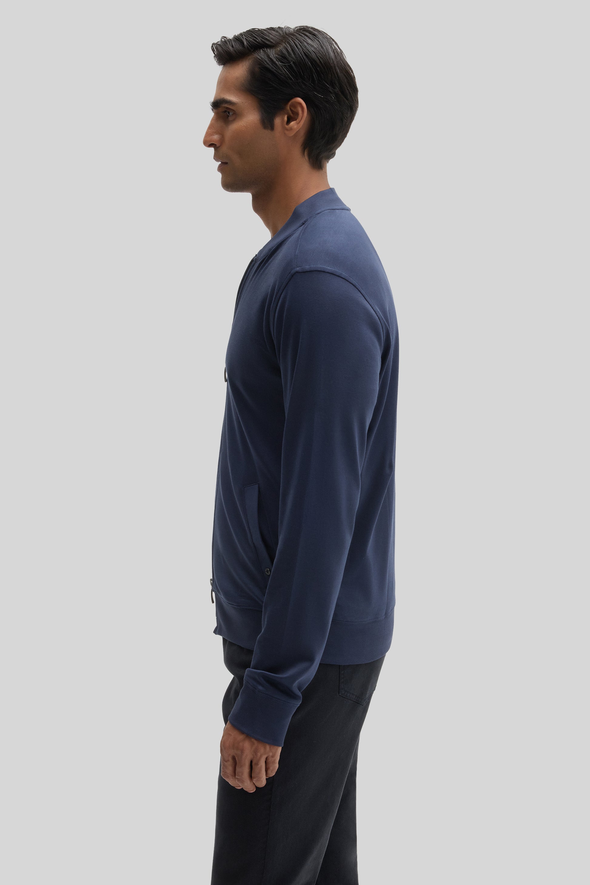 Man wearing navy blue baseball jacket with black pants, shown in side profile.