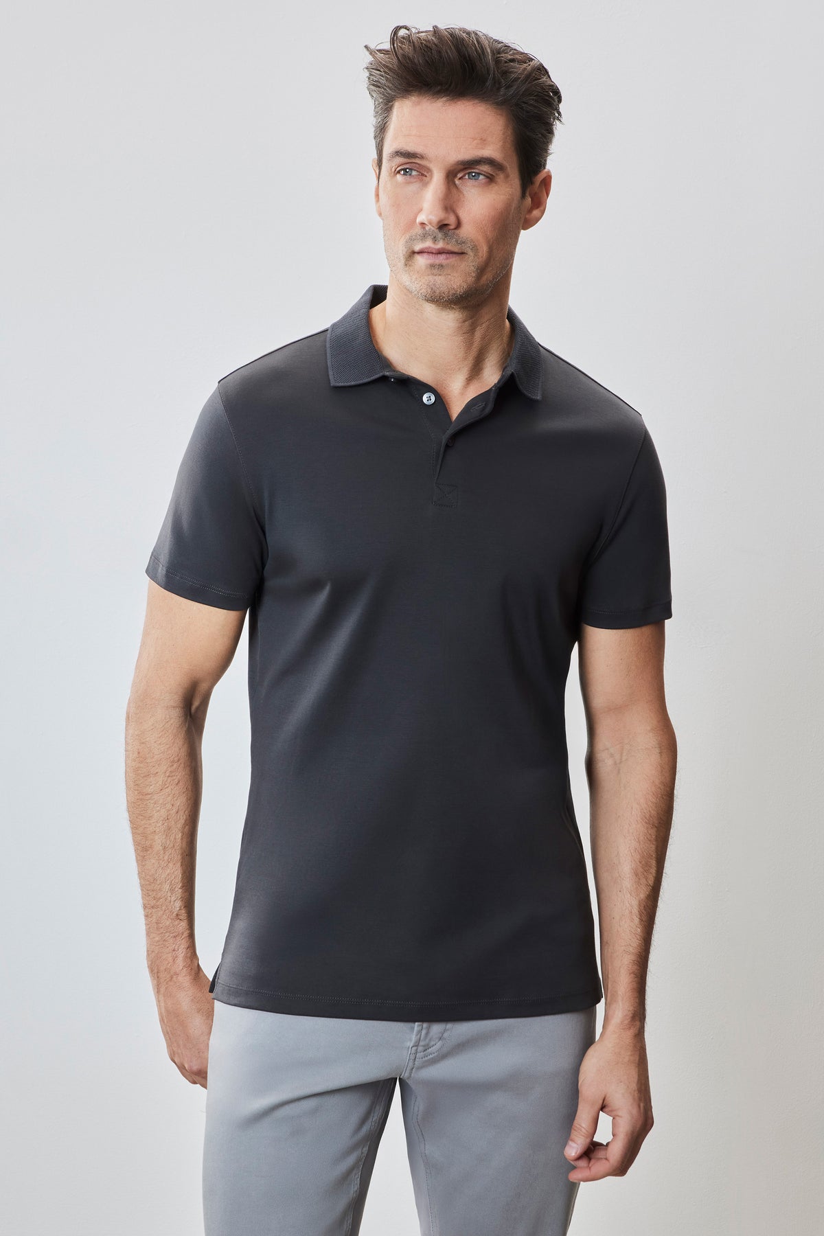 Man wearing black short-sleeve polo shirt with white button placket and light gray pants.