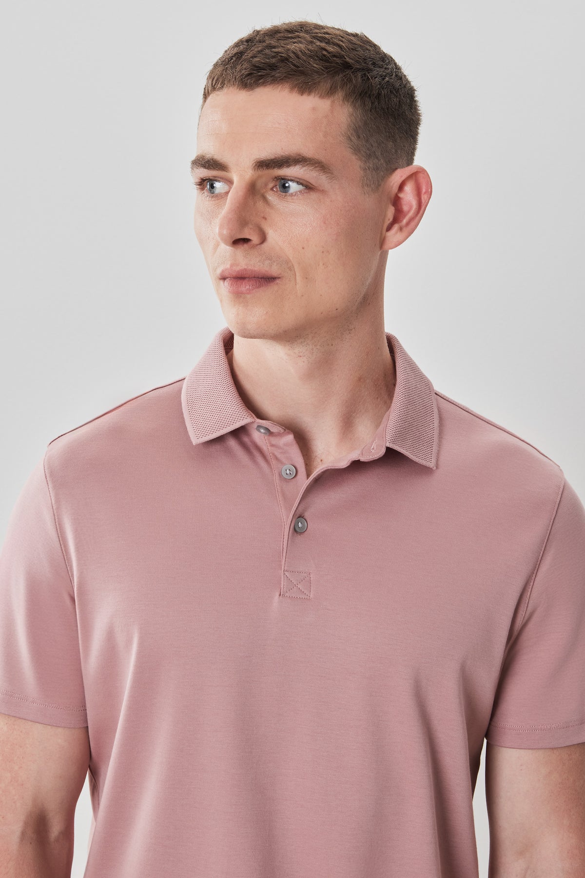 Man wearing a pink polo shirt with a textured collar and button placket.