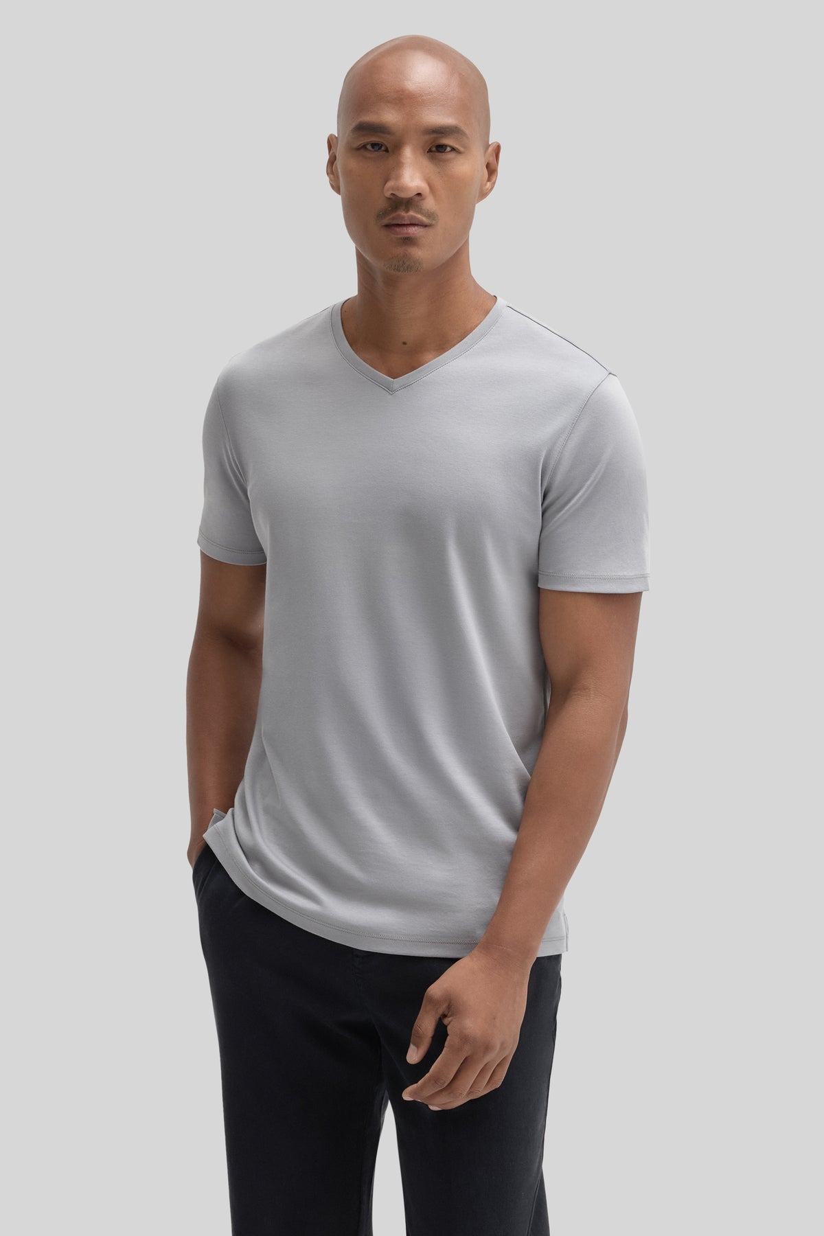 Man wearing light gray V-neck short-sleeve t-shirt with black pants.